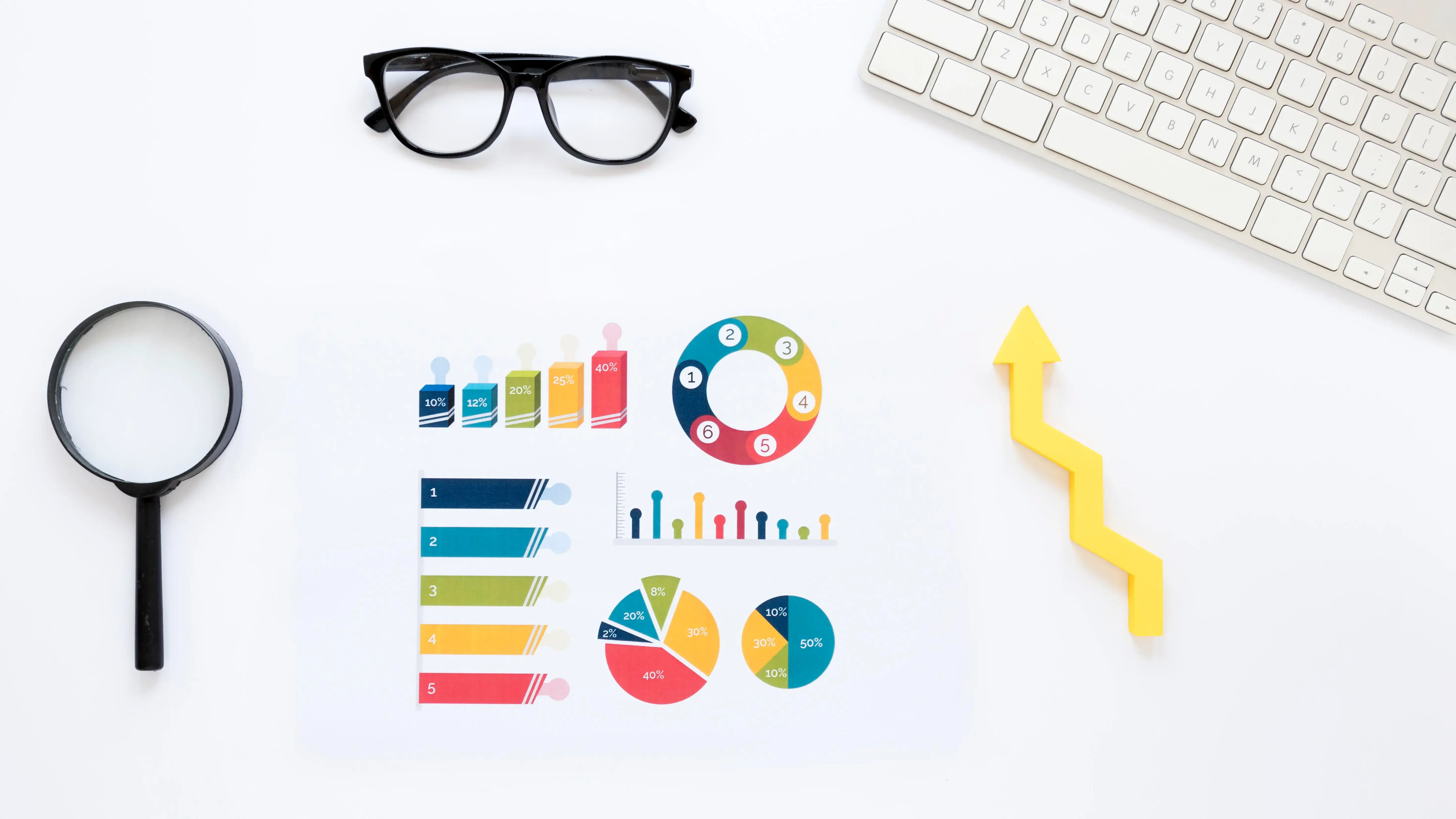 Flat lay of charts and graphs representing data analysis and business growth, with a keyboard, glasses, magnifying glass, and an upward arrow.