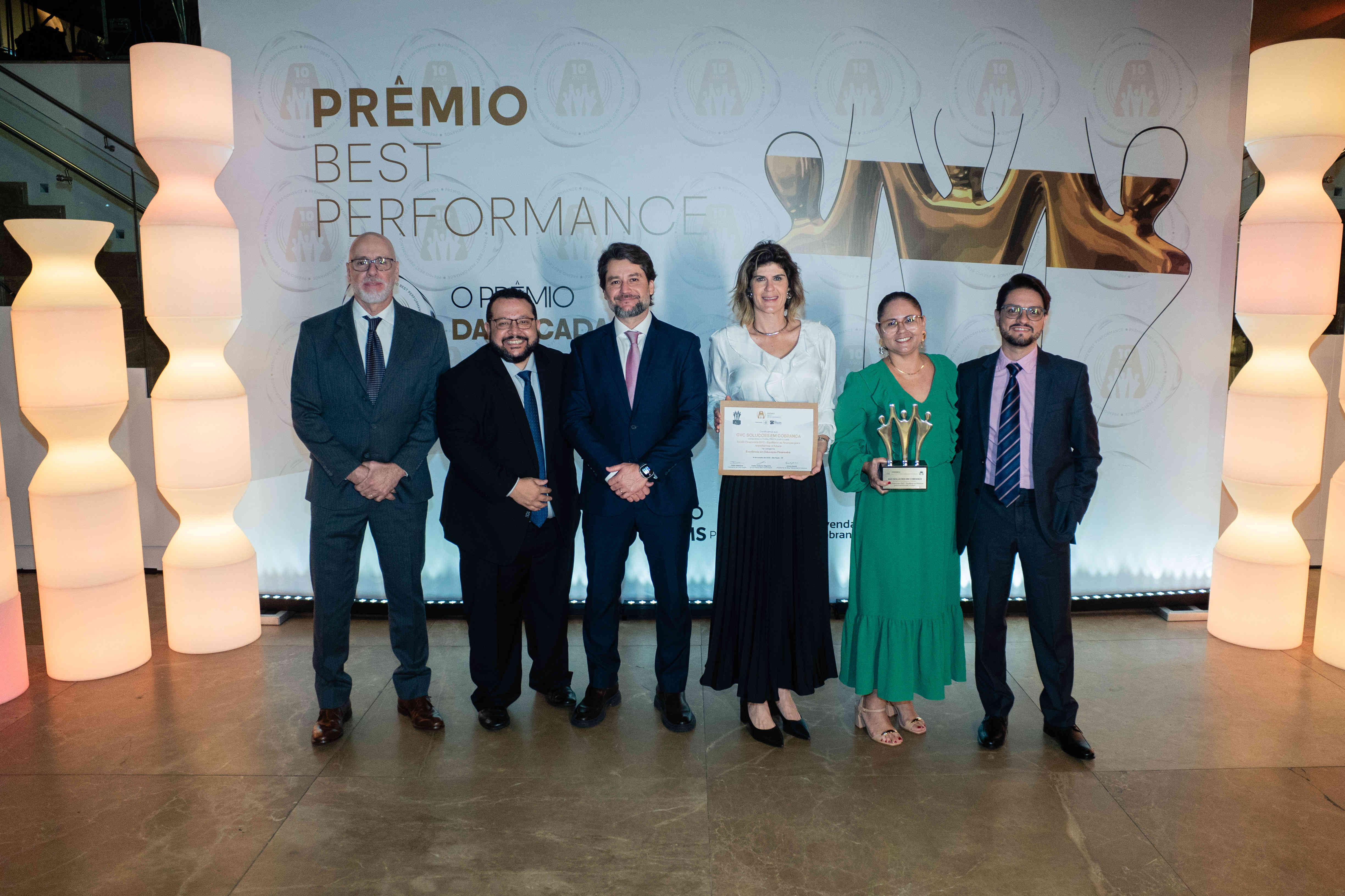 Executivos da GVC posando com troféu prata e certificado no palco do Prêmio Best Performance 2025