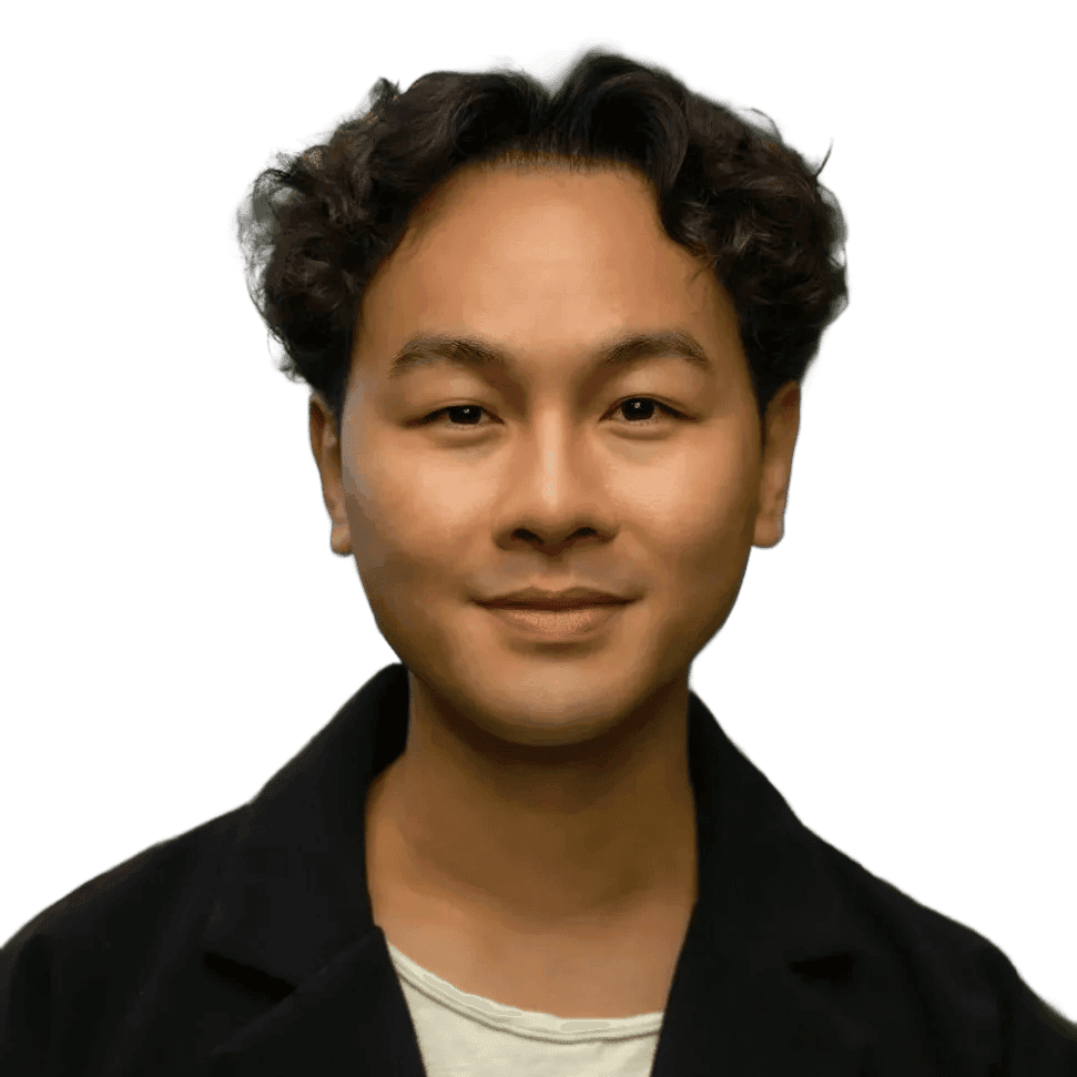 Retrato de uma pessoa com cabelo curto, escuro e ondulado, vestindo uma jaqueta preta sobre uma camisa clara, de frente para a câmera com um leve e tranquilo sorriso, contra um fundo escuro.