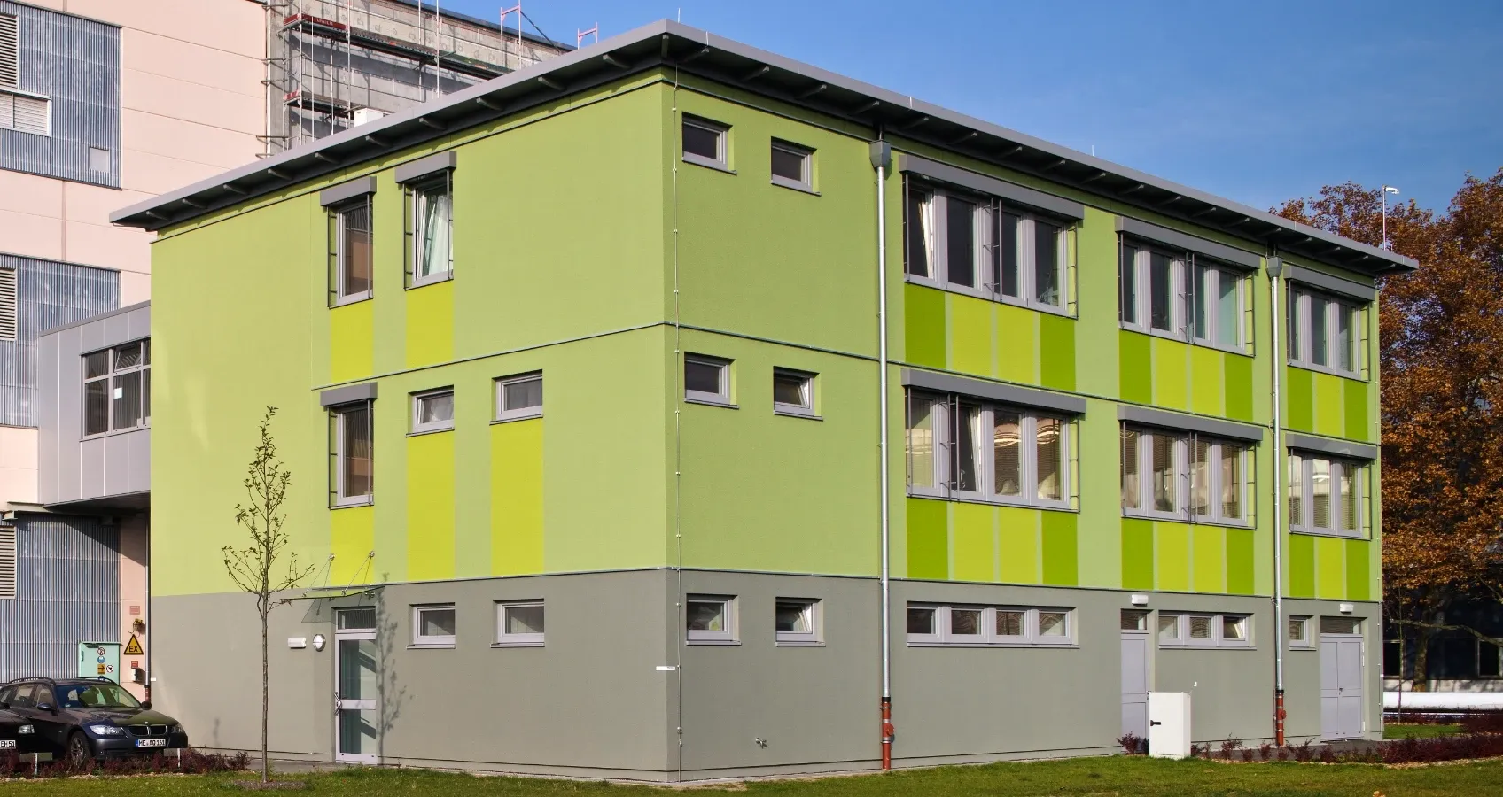 Modern zweistöckiges Gebäude in hellen Grüntönen mit grauem Sockel, vielen Fenstern und vertikalen Streifen.