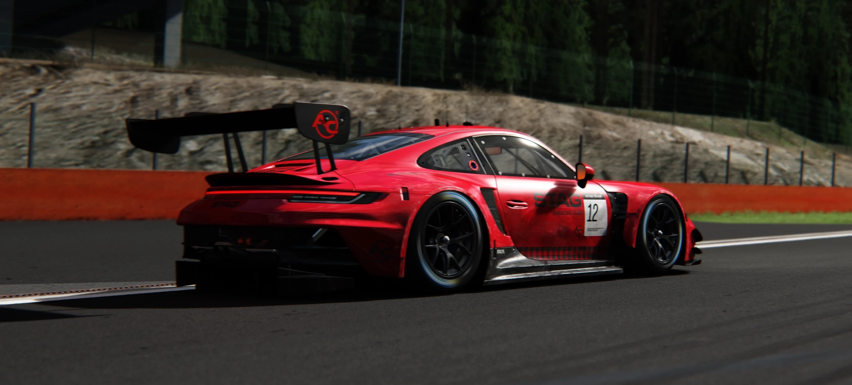 Red sports car with number 12 and ‘STAG Racing Team’ branding on a racetrack, featuring a large rear wing and black rims.