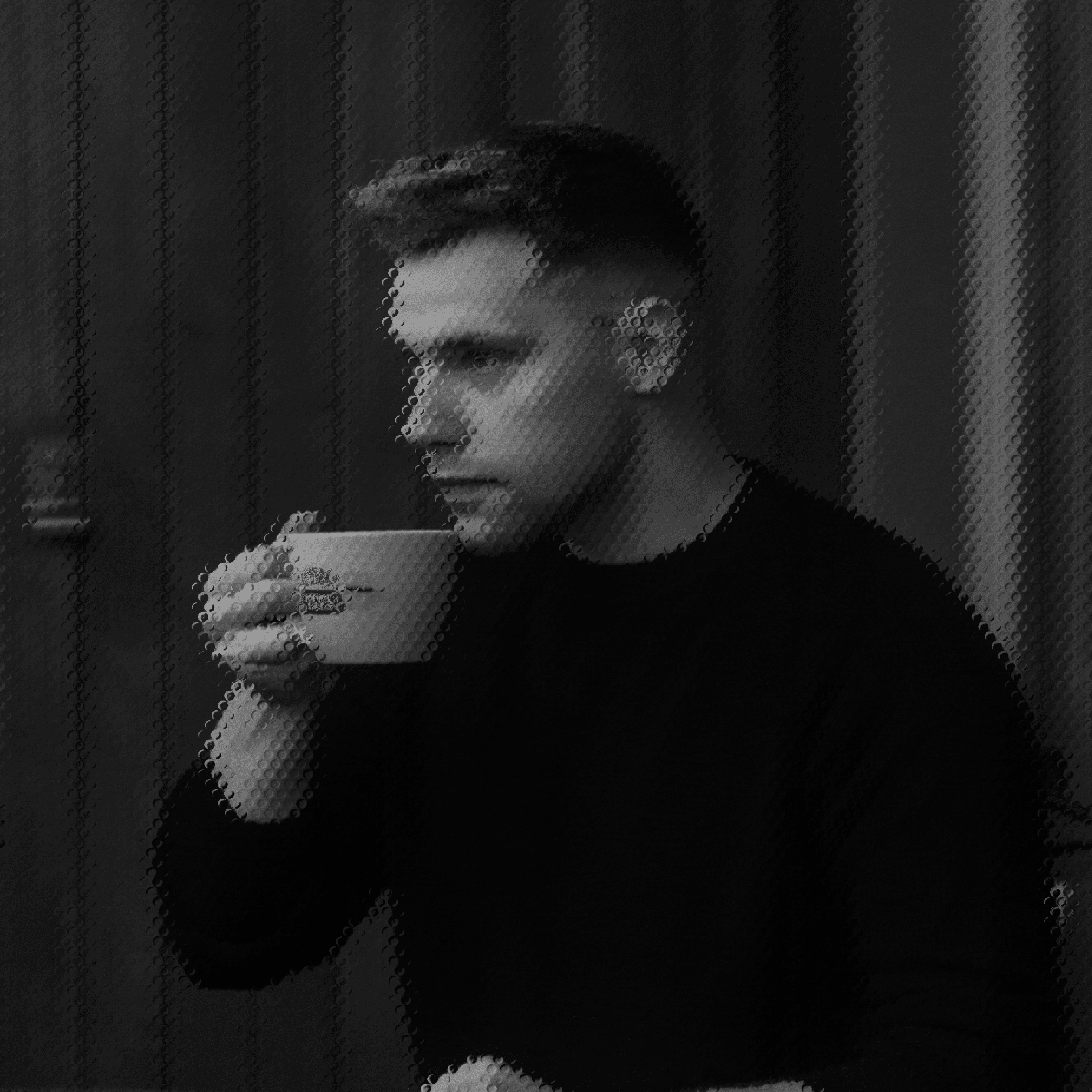 A person in a dark sweater sits indoors, sipping from a ceramic mug, with a focused expression against a softly lit background.