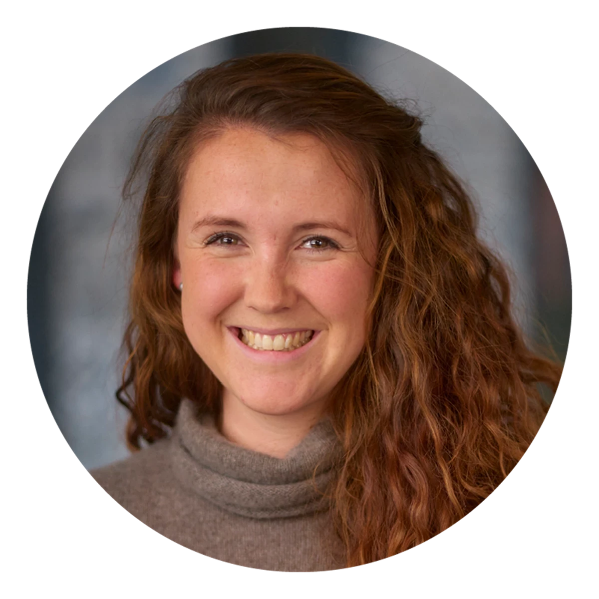 A circular portrait shows a person with long, wavy auburn hair wearing a high‑neck top. The background is neutral and studio‑style.