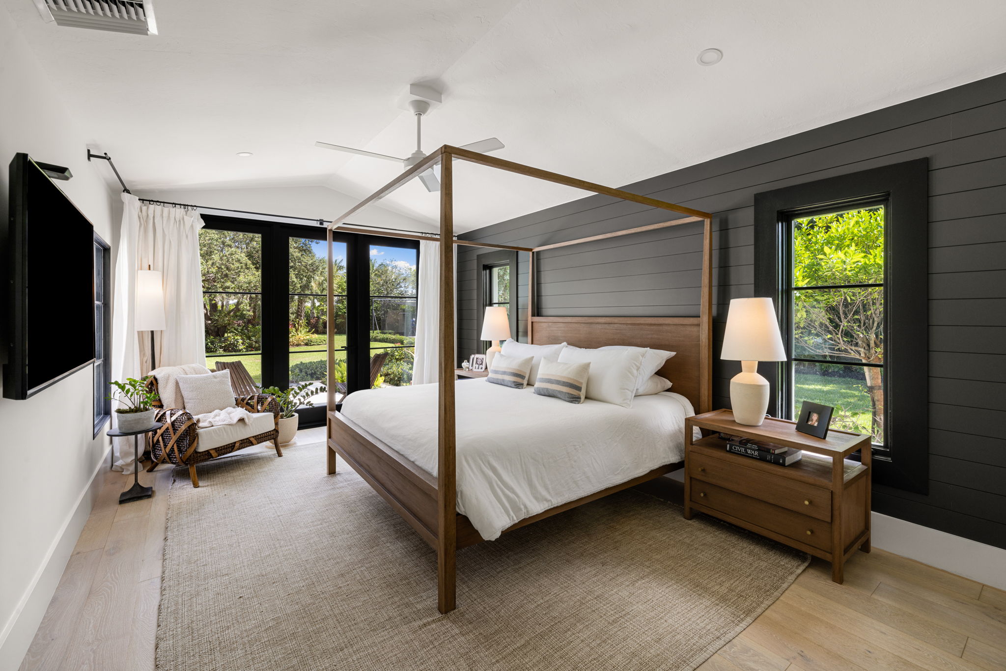 a large bedroom with black and white walls displaying a large spruce bedframe in the middle of the room and glass doors leading to the backyard