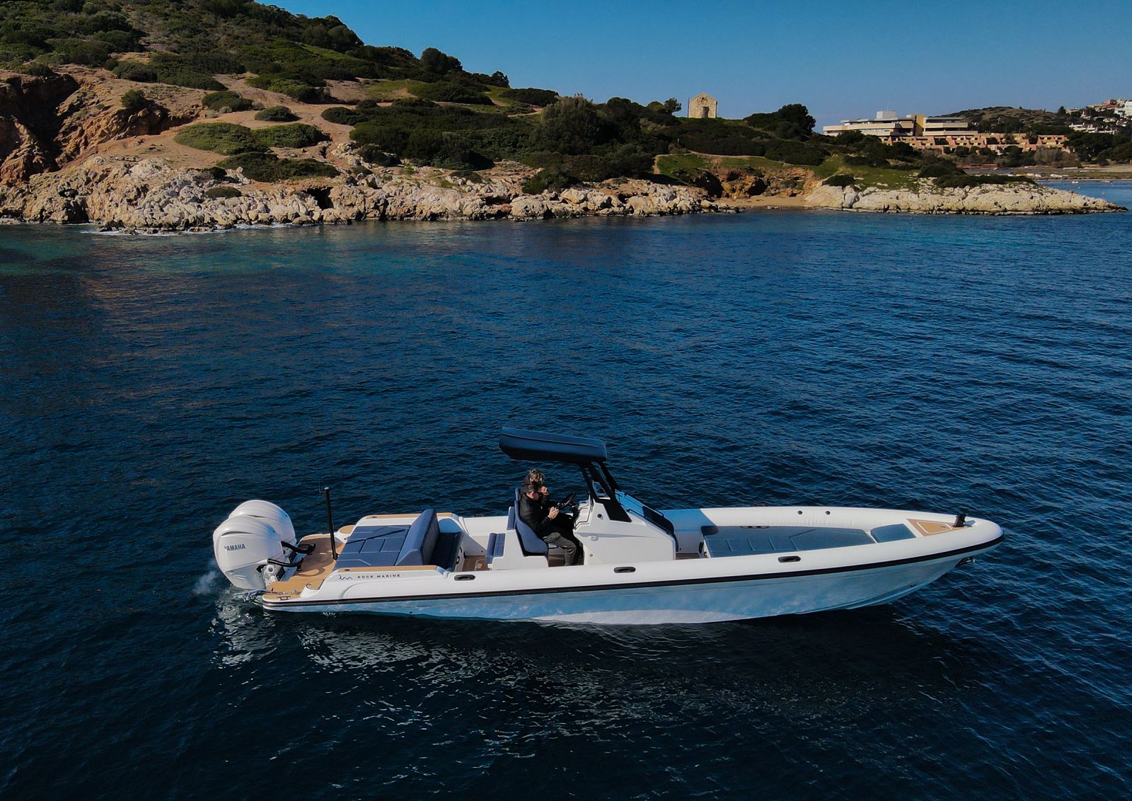 White Rock 36 speedboat with captain at helm cruising calm blue waters near Paros coastline with hills in background.