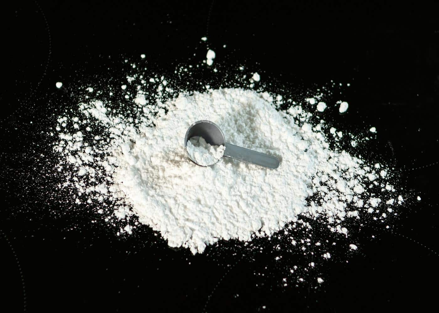 Creatine powder and a scooper on a black background