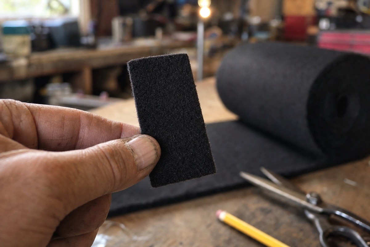 A hand-cut rectangle of black carbon felt held over a workbench