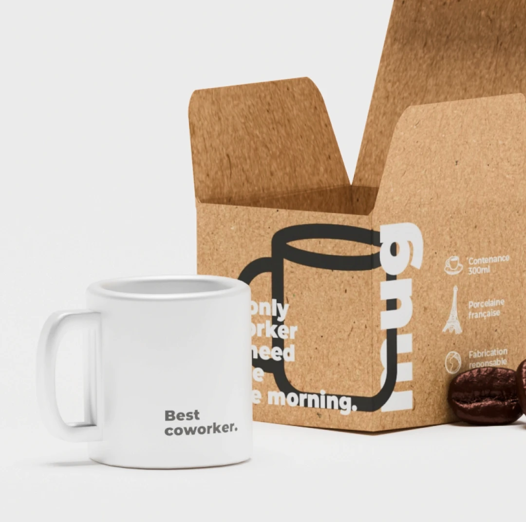 Shooting produit 3D mug "Best coworker" posé avec packaging kraft ouvert — pictogrammes produit visibles (300ml, porcelaine française, fabrication responsable), rendu studio virtuel, Tartelette Concept