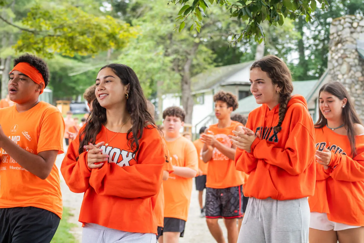 Campers in orange Lenox shirts clapping together at Camp Lenox