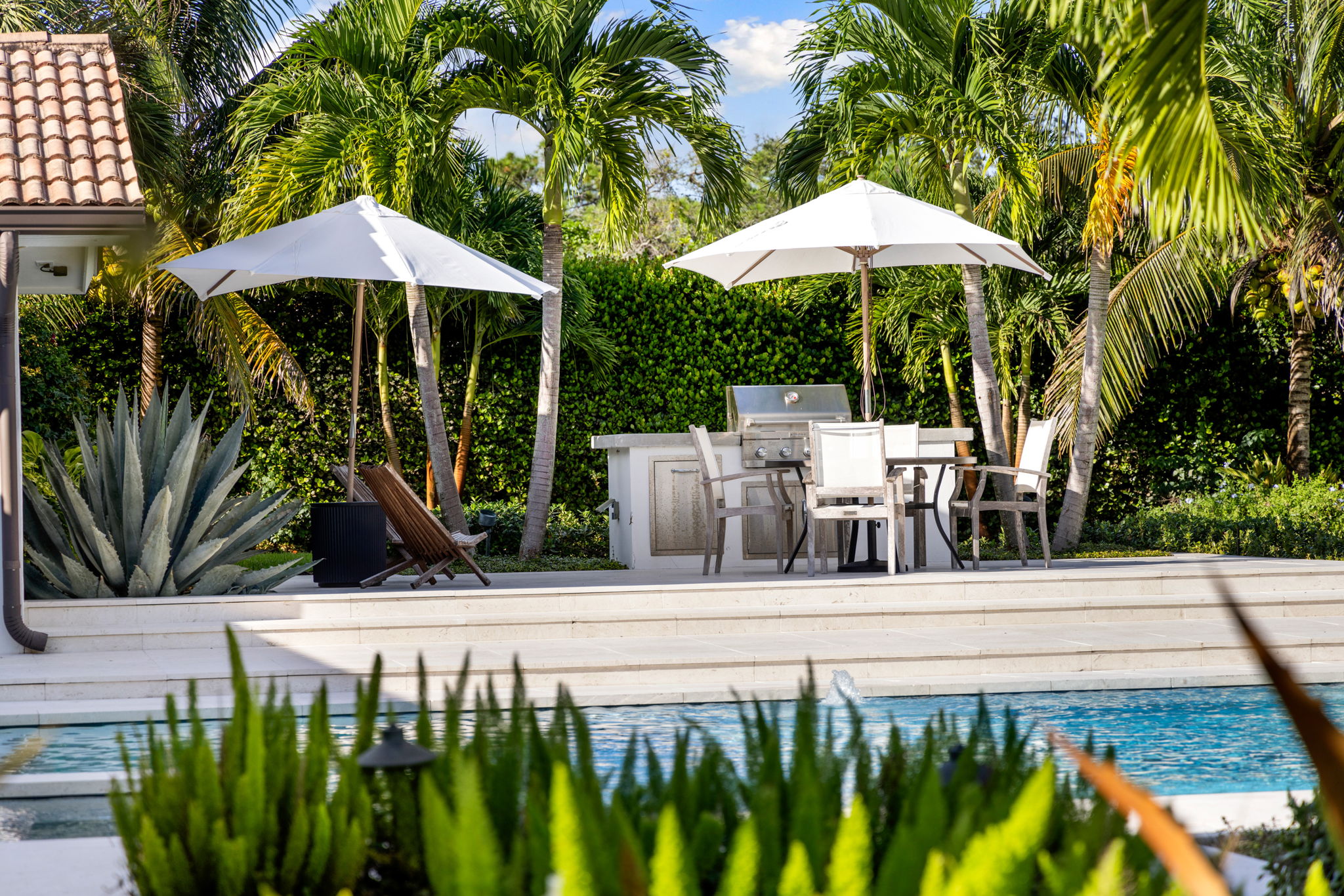 a large outdoor area with tables covered by umbrellas and palm trees and other plants in the background