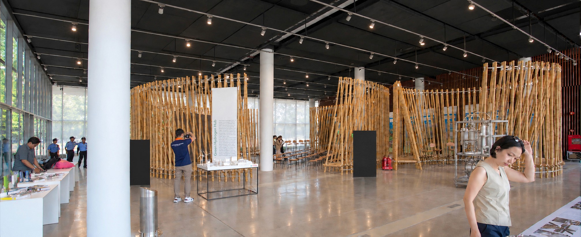 Blick durch die Halle auf die Bambusinstallation, Besucher an Tischen im Vordergrund