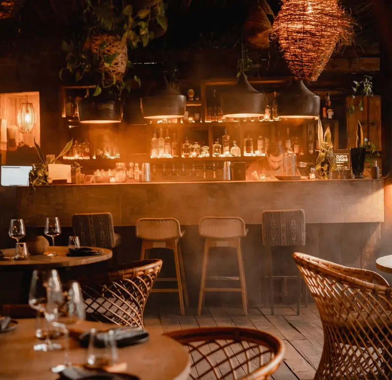 Nighttime ambiance at Jungle Bar, Be Tulum, featuring tables, chairs, and bartender at the bar.