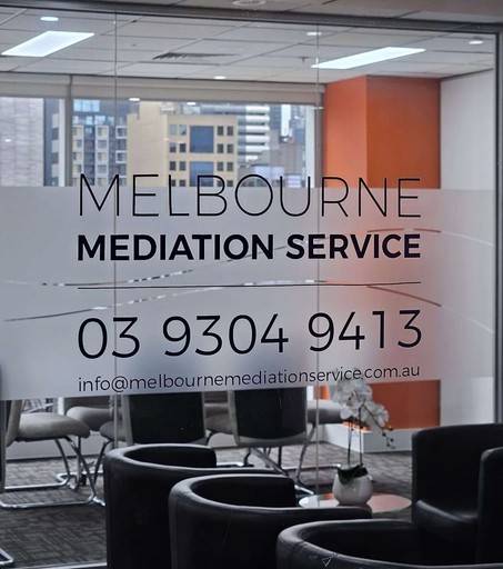 The entrance to Melbourne Mediation Service, featuring the services' contact details and conferencing rooms in the background, nearby a waiting room with four seats in view.