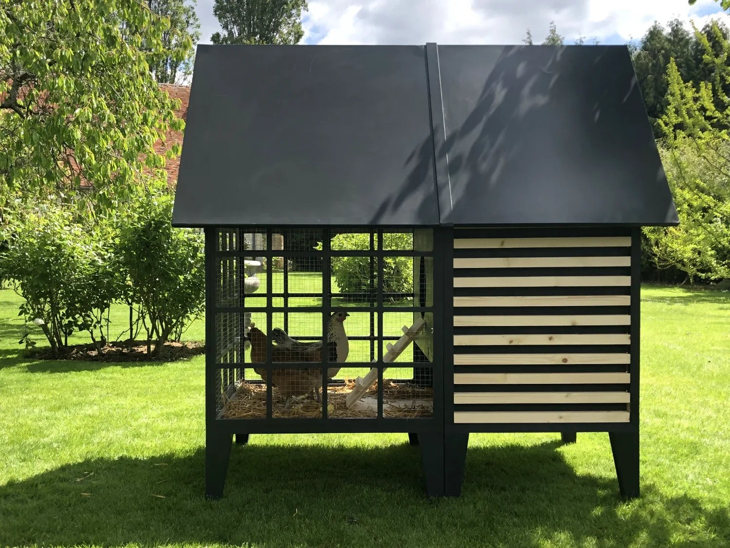Poulailler Gallina Copacabanon en bois et métal noir avec poule à l'intérieur, dans un jardin soigné
