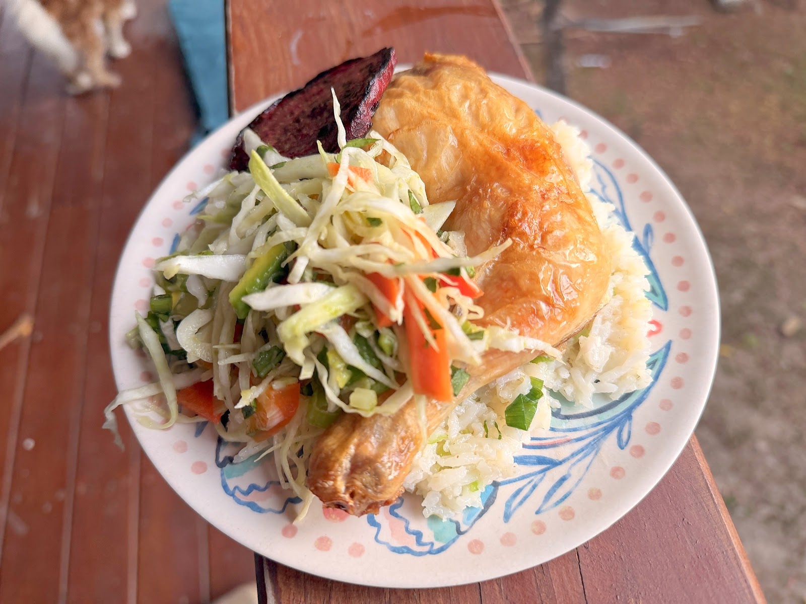 A plate of roast chicken, rice, fresh cabbage slaw and roasted sweet potato on an outdoor table in Roatán