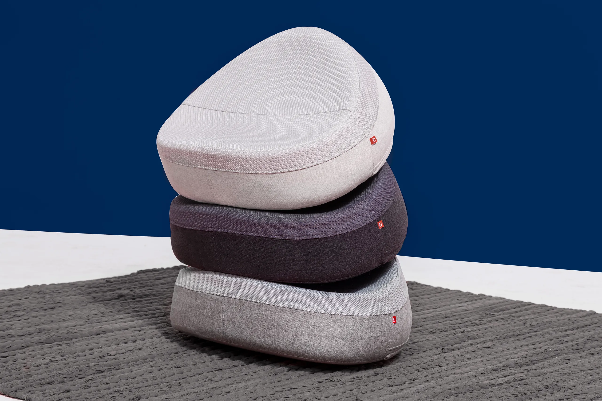 Three UNDO meditation cushions stacked in white, dark gray, and light gray