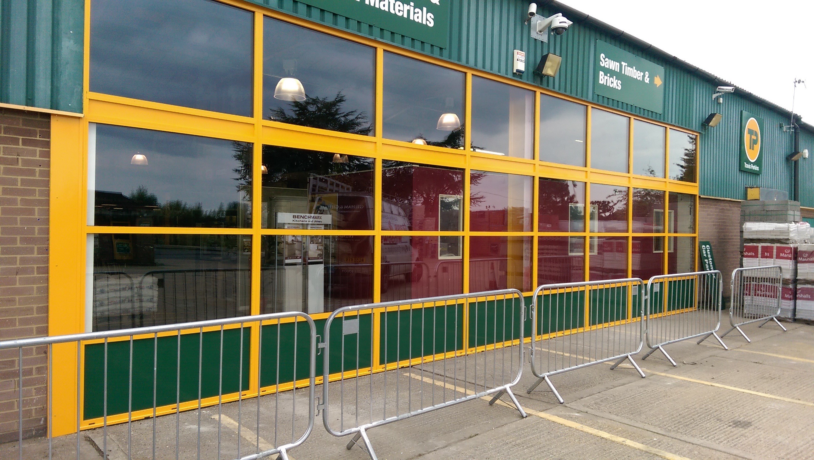 The same shopfront after replacement: a new powder coated aluminium shopfront screen in yellow, glazed throughout, in front of the open branch