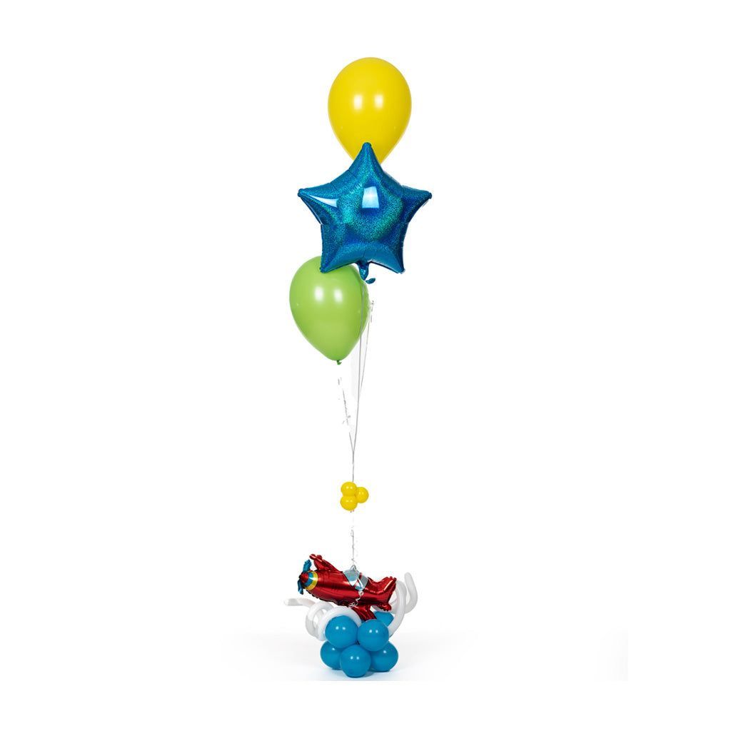 Colorful helium balloons, including a yellow round, green round, and blue star-shaped balloon, are attached to a vibrant floral arrangement with blue base balloons, creating a festive and joyful centerpiece.