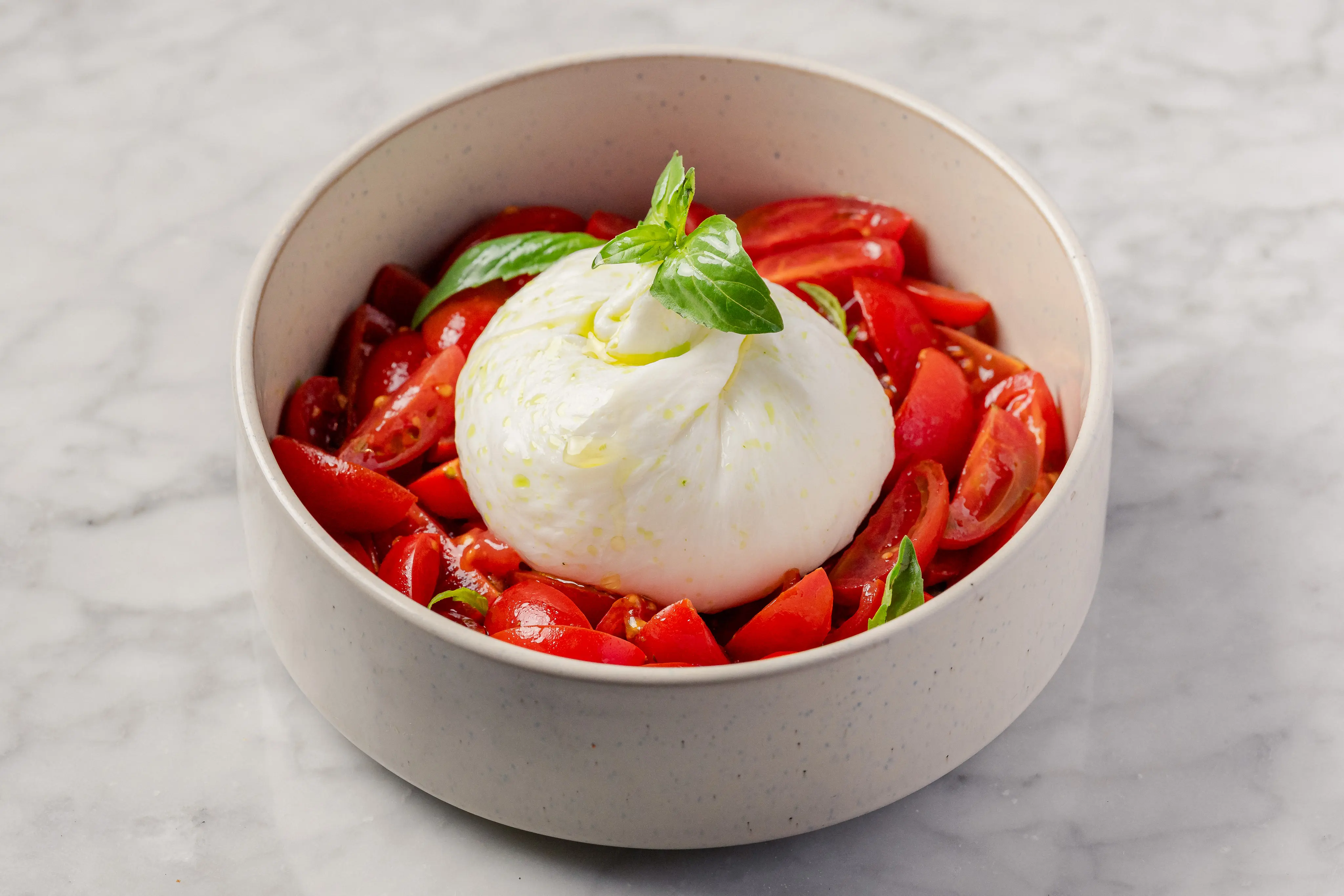 Burrata caprese salad recipe served at O Ver Borough, featuring a whole creamy burrata on Sicilian Datterino tomatoes with basil and olive oil in a ceramic bowl