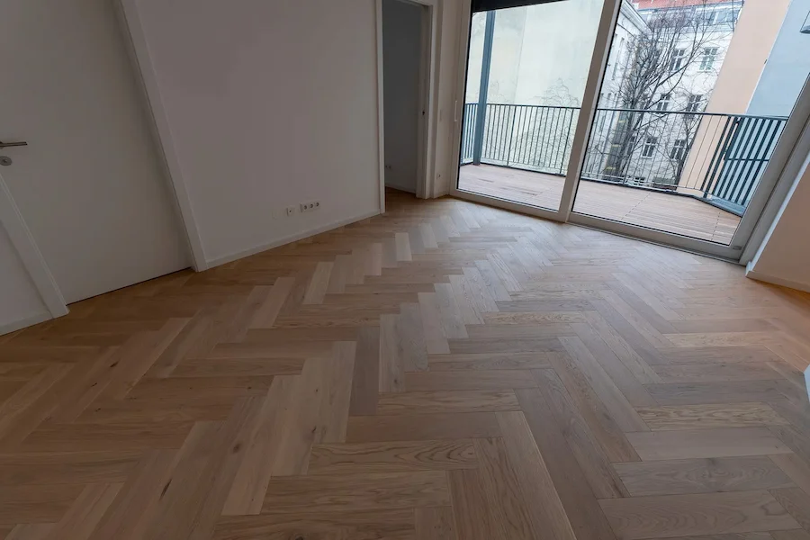 Zimmer mit großer Glasfront und frisch verlegtem Fischgrät-Parkettboden in warmem Holzton.