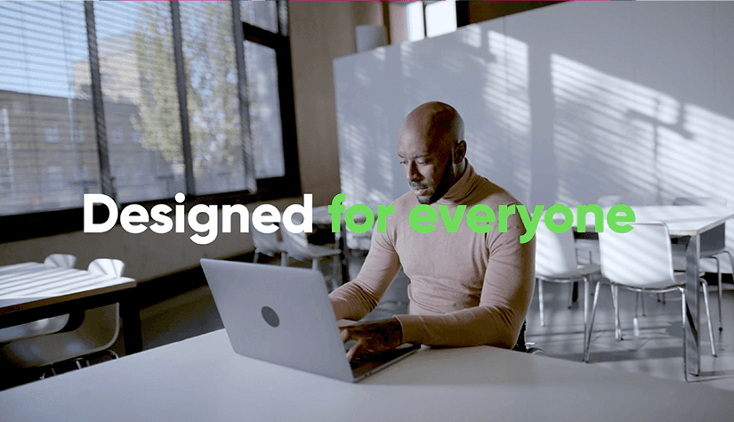 A man at a desk working on a laptop in a stylish workplace canteen with the caption 'Designed for everyone' - the image is a still from a communications film we created for the technology company ServiceNow