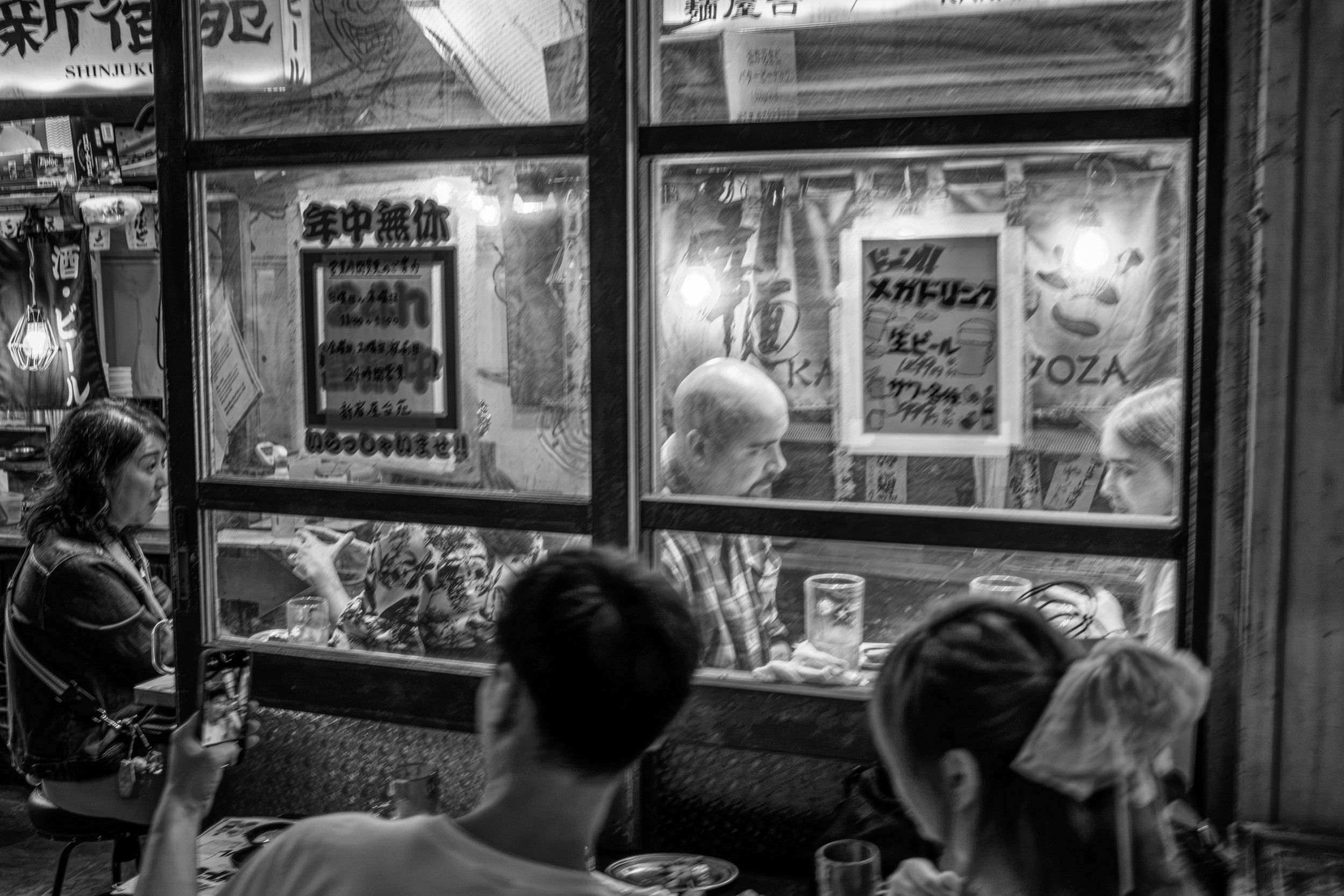 Black and white night photograph of diners eating and drinking inside a small izakaya.