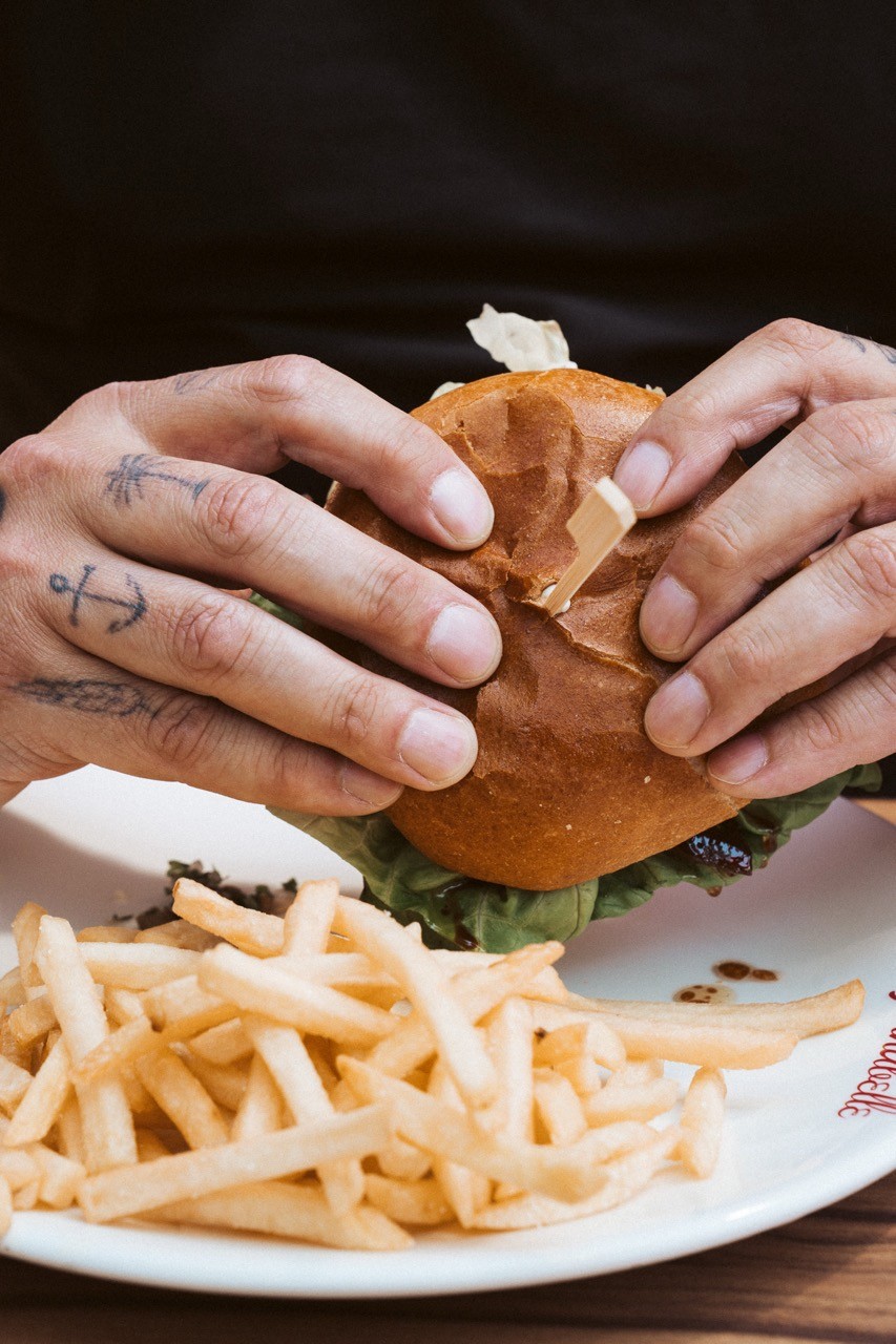 person with tattoos on his hands eating a burger and fries