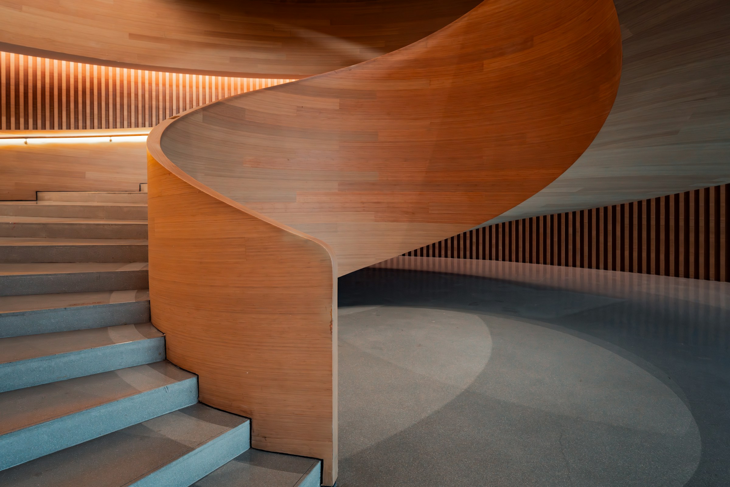 Minimalist interior with curved steps, arched doorway, and modern black chair. Textured beige walls and soft lighting create a serene ambiance.