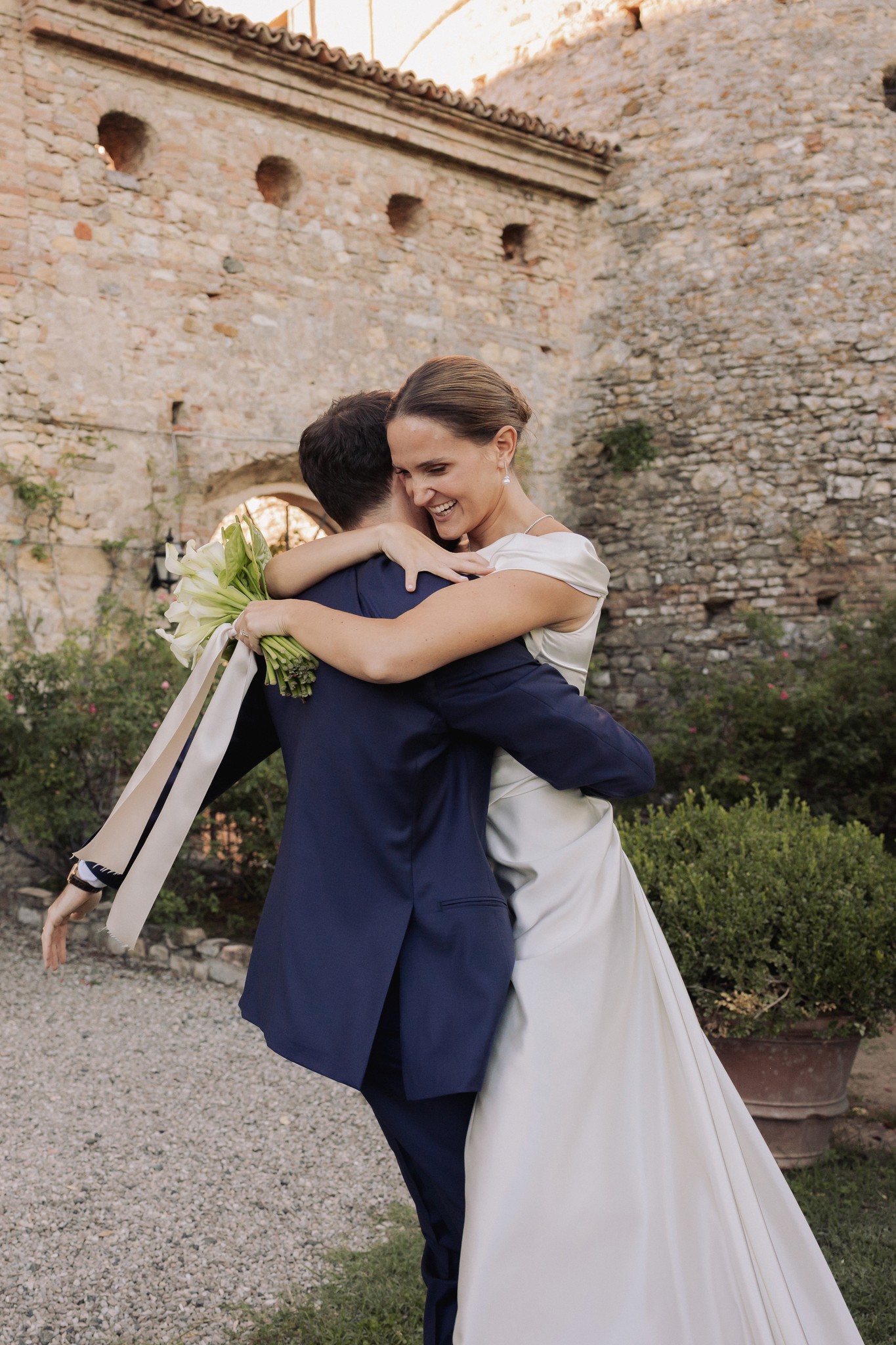 Sposi si abbracciano ai muri medievali del Castello di Scipione, abito bianco e bouquet, reportage di matrimonio