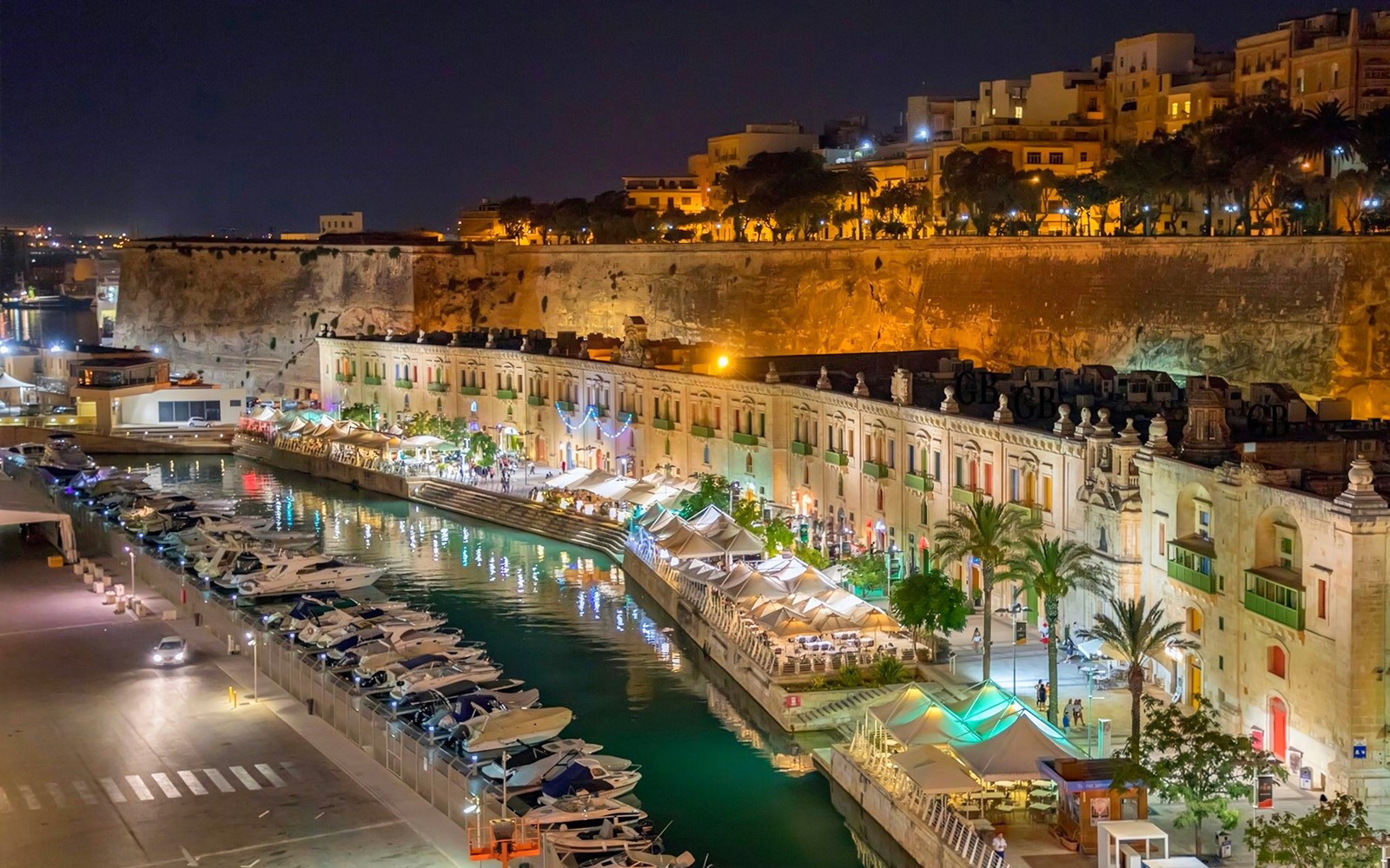 Night view of Valletta waterfront with boats and illuminated buildings, Malta.