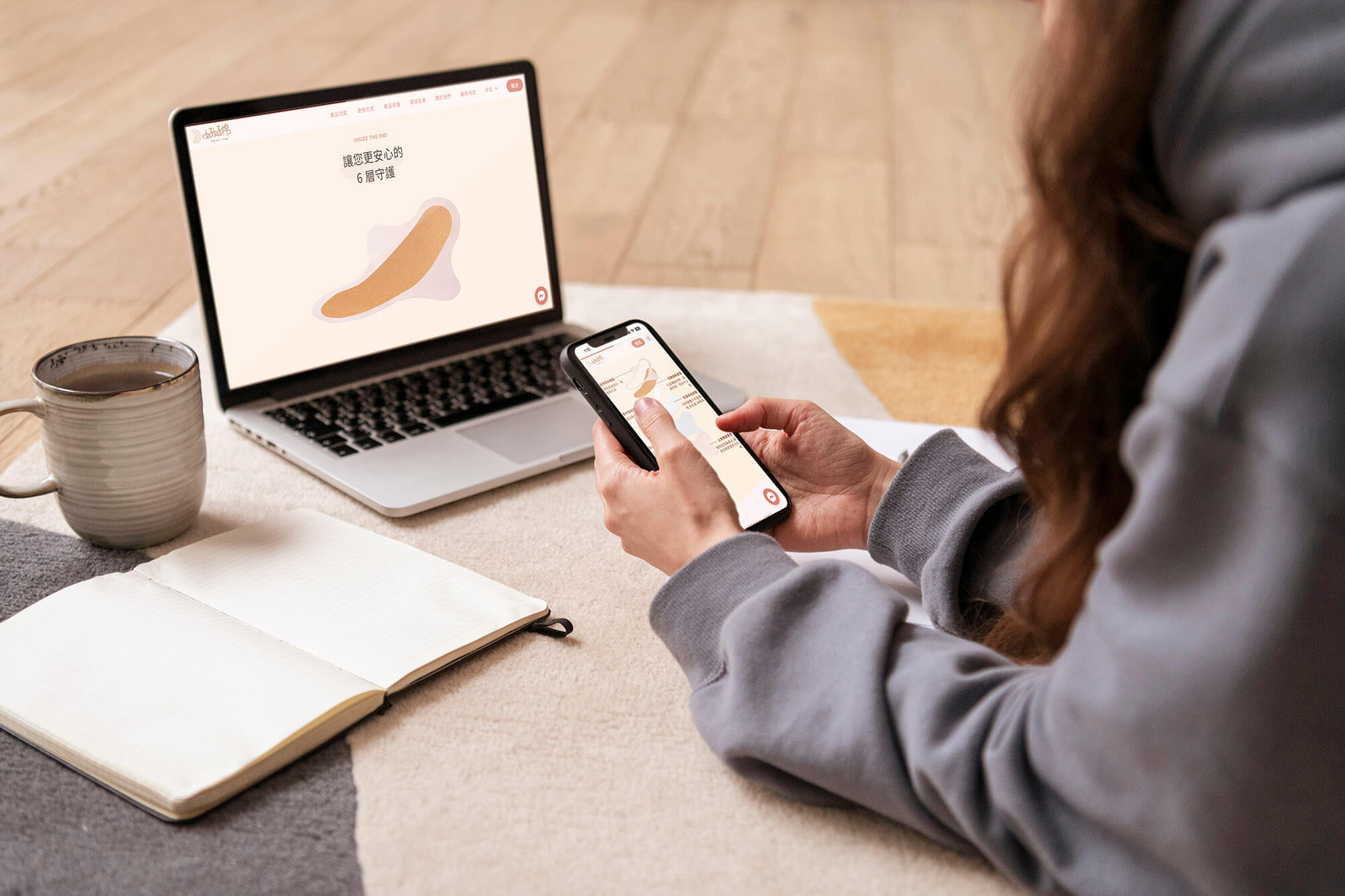 這張圖片展示了一位女性坐在地毯上,在電腦上查看好好棉的網站。