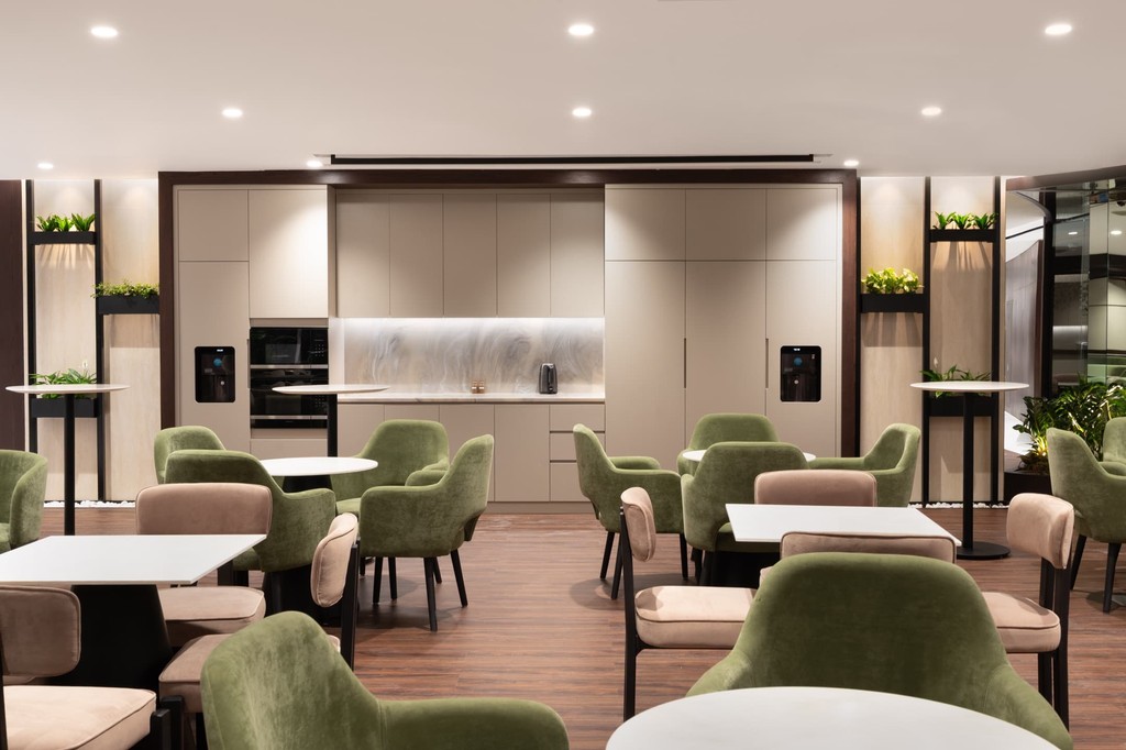 Relaxed lounge zone in serviced offices in Dubai with soft green seating, round tables, and a built-in coffee bar.