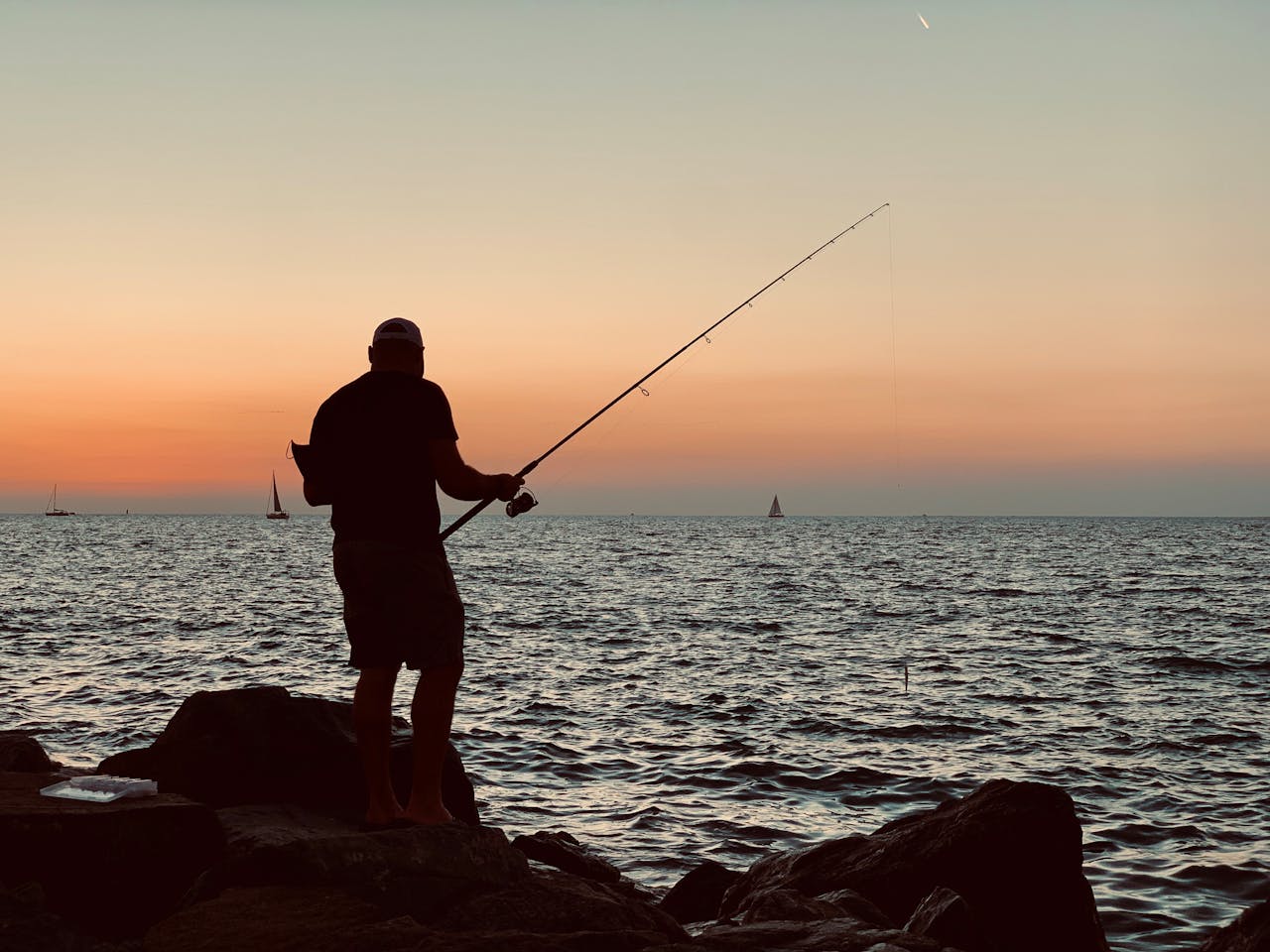 A man fishing by the rocky coast in Dubai at sunset, a popular fishing activity in Dubai.