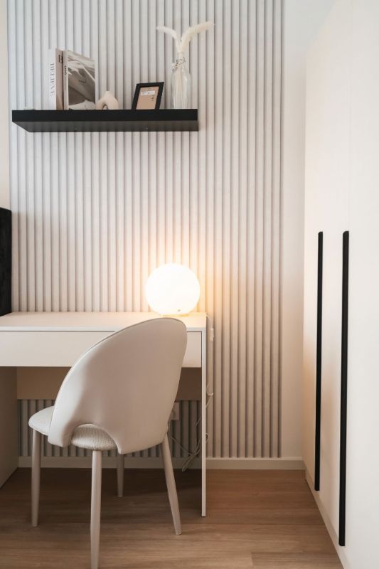 Minimalist Airbnb bedroom work nook with globe table lamp and white fluted wall panel — short-term rental interior photography