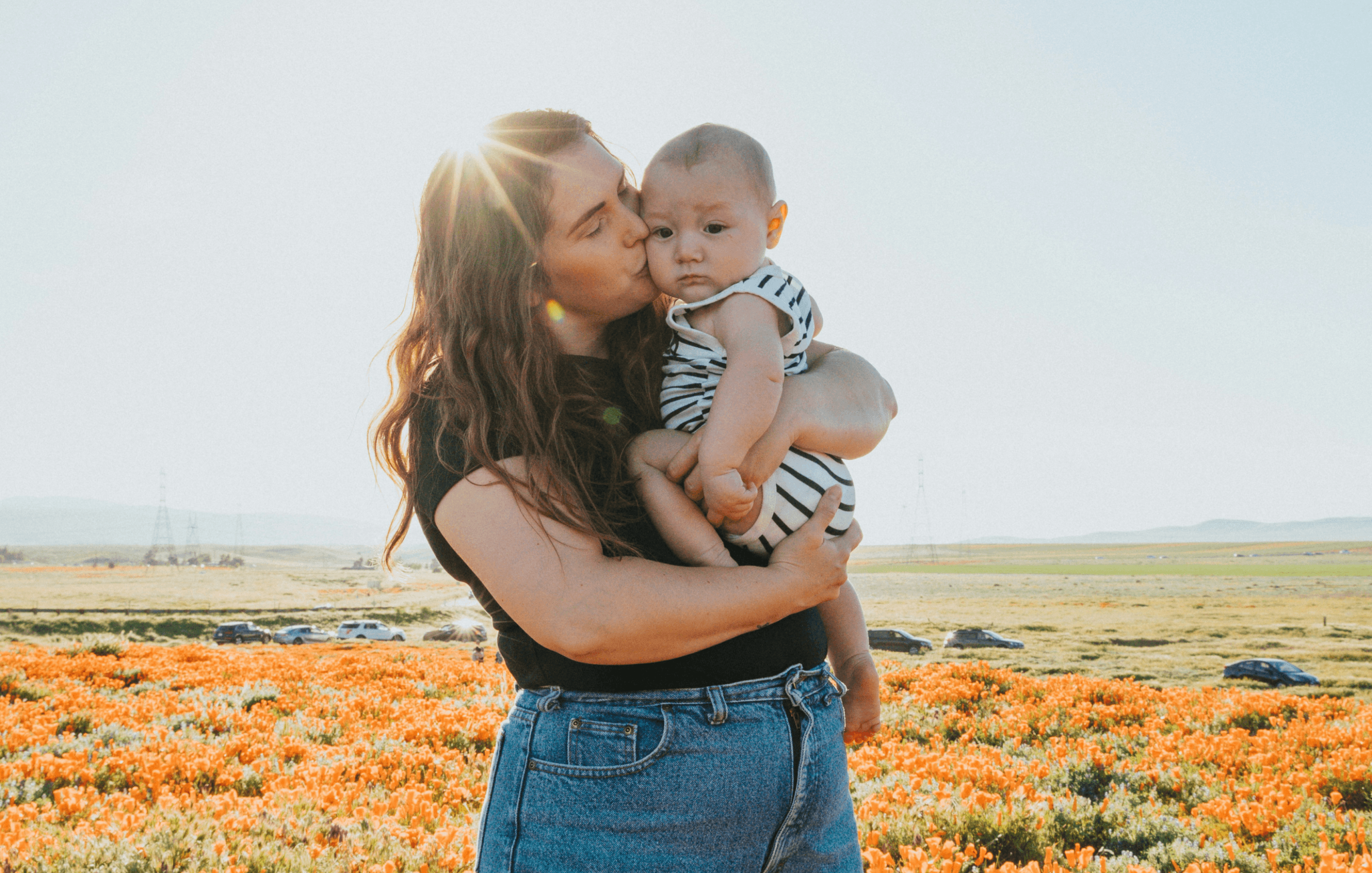 Mère embrassant son bébé dans un champ de fleurs au coucher du soleil