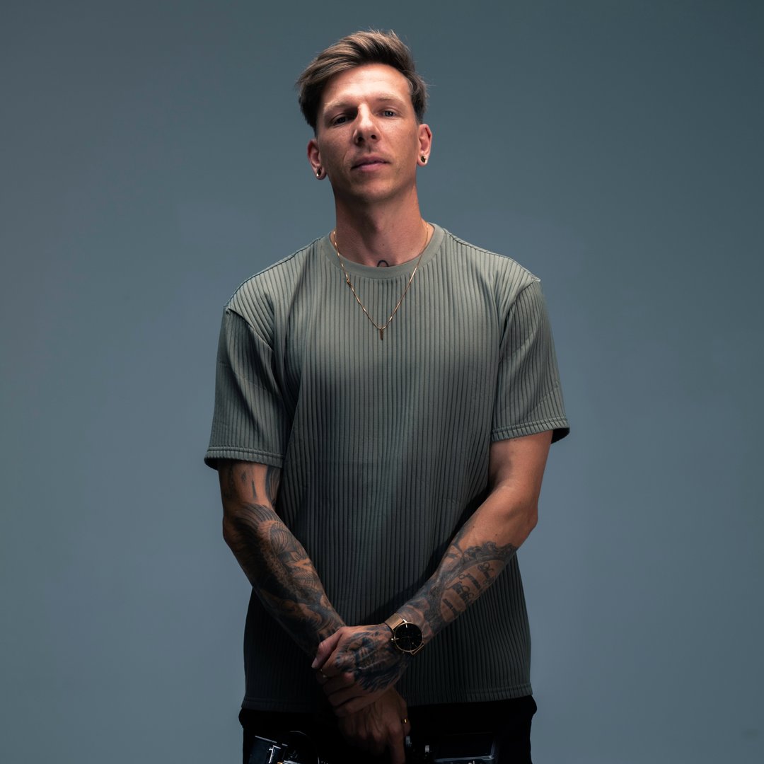 A confident person with short, styled hair and a leather jacket poses against a dark backdrop.