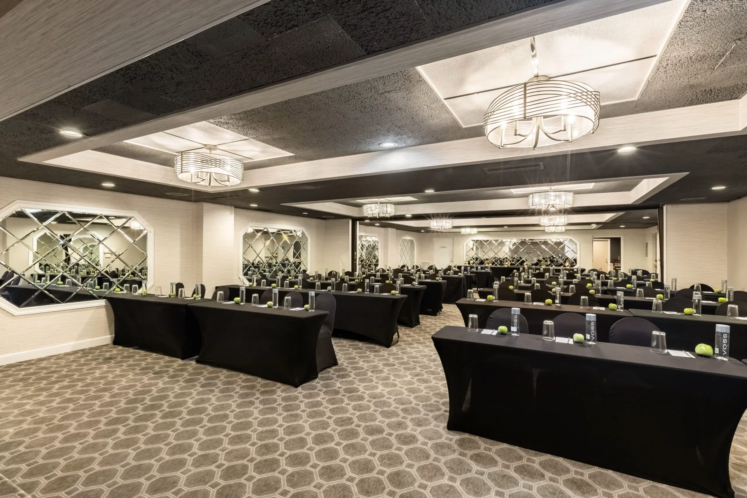 Empty conference room with black tables, chairs, water bottles, and apples.