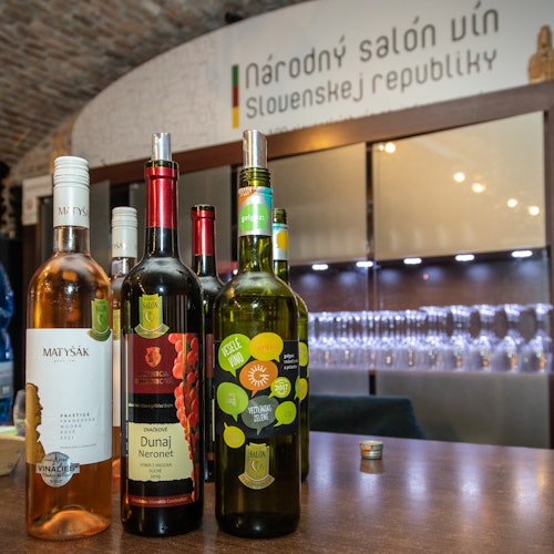 Cuatro botellas de vino sobre un mostrador frente a un cartel que dice "Národný salón vín Slovenskej republiky."