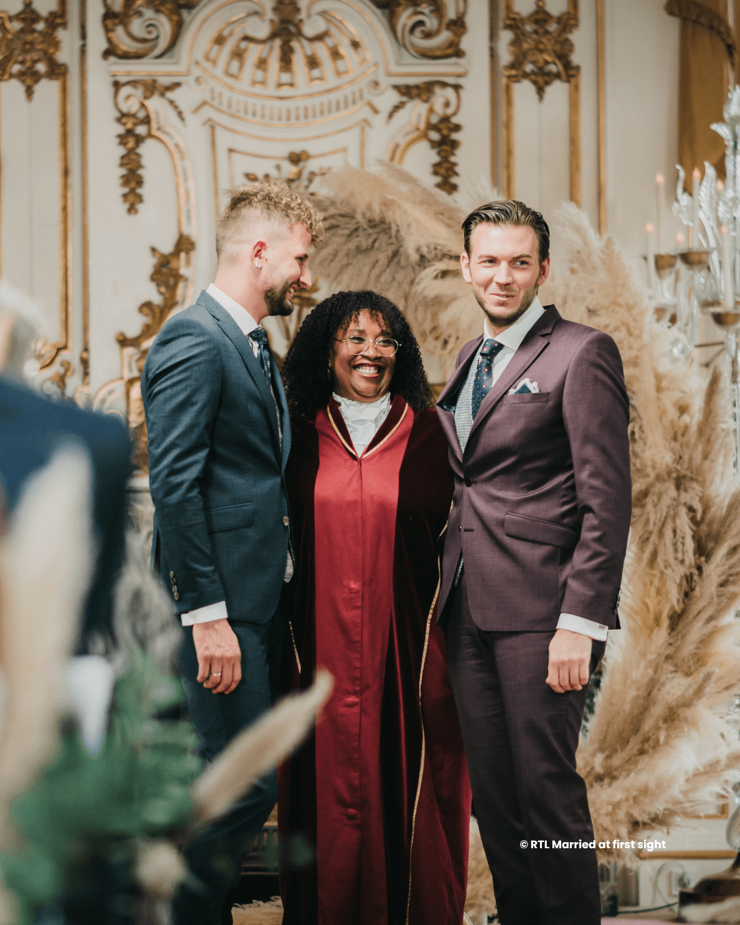 Drie mensen staan samen, gekleed in formele kleding, tegen een elegante achtergrond met decoratieve details het is een stijlvolle gay bruiloft vol liefde en elegantie.