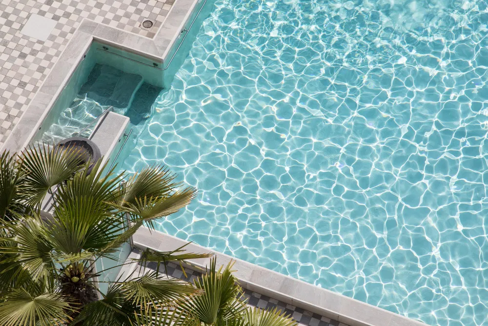 Aerial view of a sunlit swimming pool with shimmering water and palm trees along the edge.