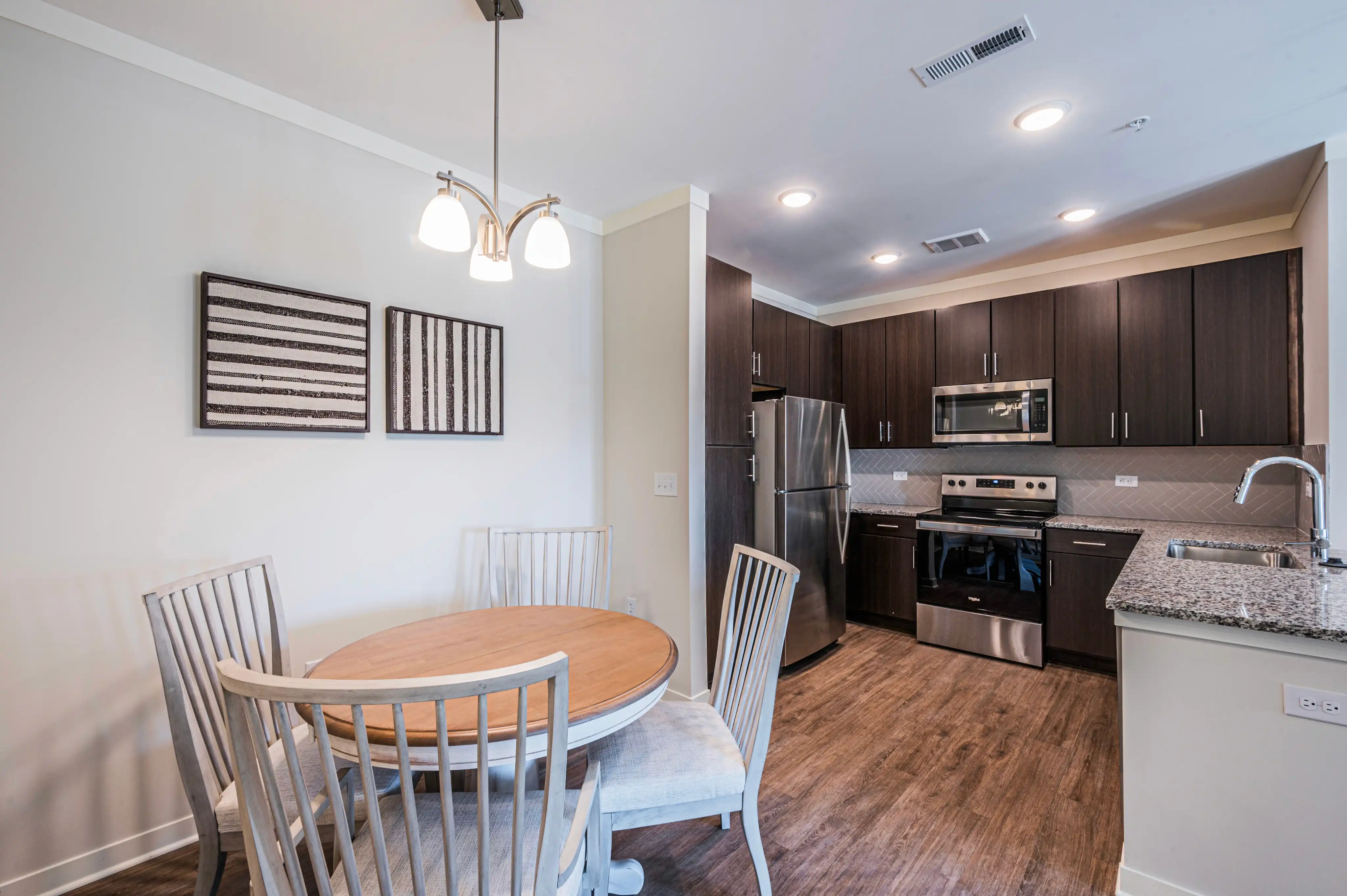 Furnished apartment dining area and kitchen with a round table, dark wood cabinets, and granite countertops at The Reserve at Cool Springs, Elizabethtown, KY