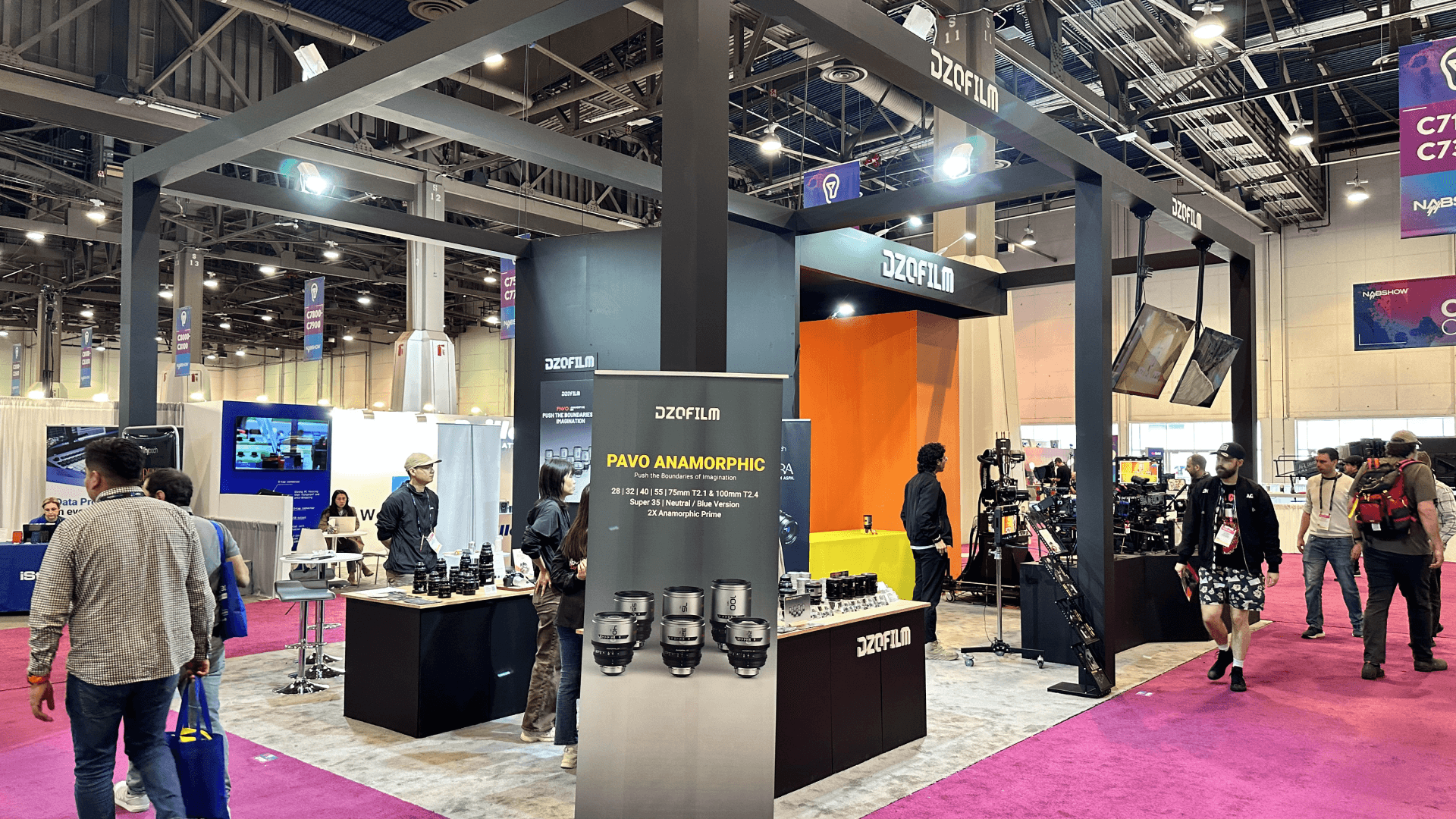 Open layout showing attendees interacting with Pavo Anamorphic lenses on wooden display tables.