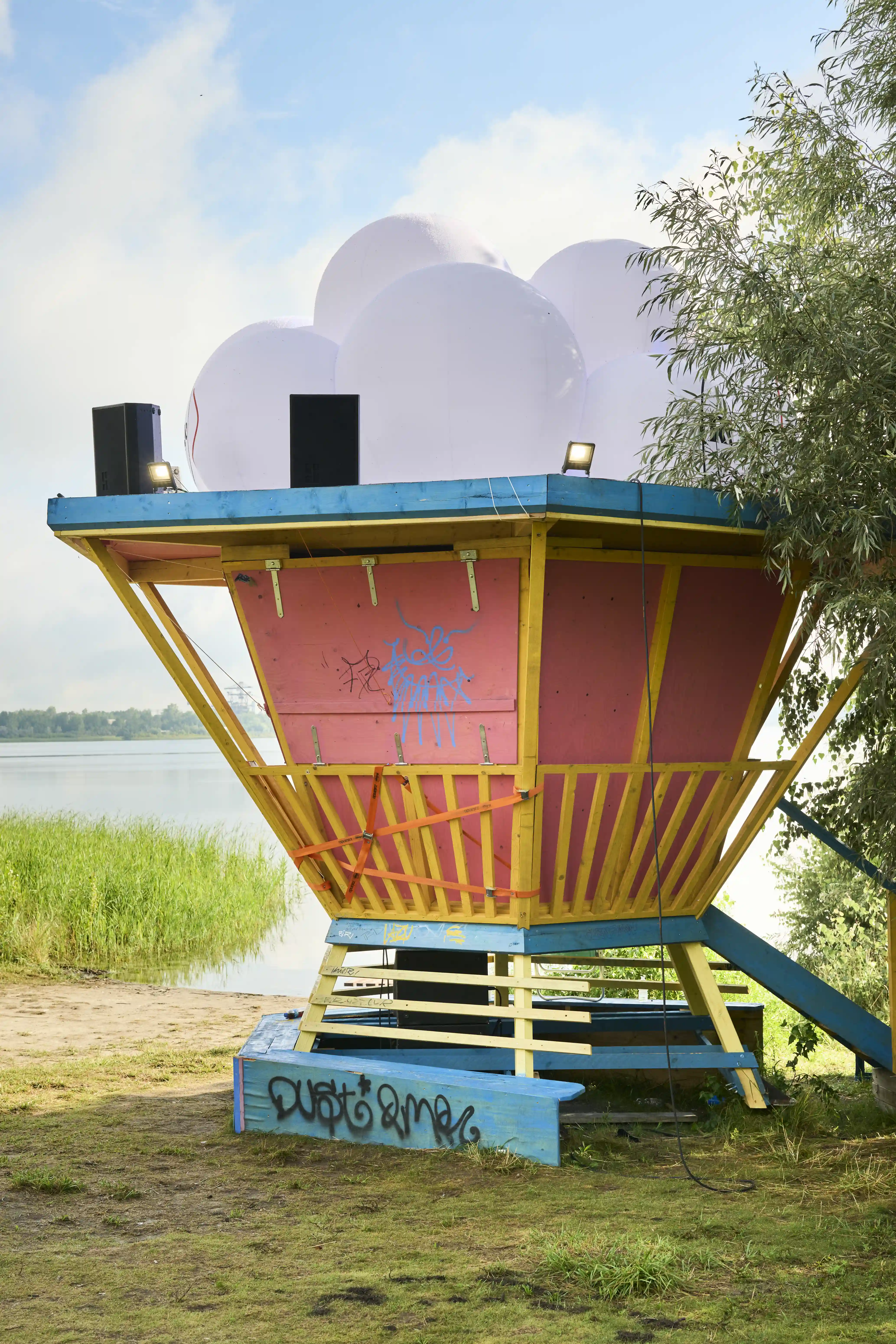 Colourful wooden DJ tower with balloon spheres and speakers by the lake at Melt Festival.