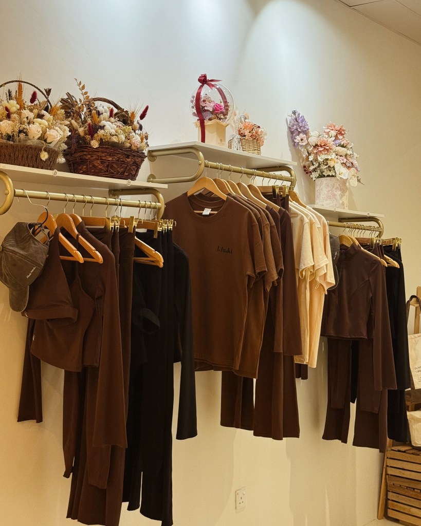 Clothing display featuring brown and black apparel on hangers, with decorative baskets of flowers on shelves overhead.