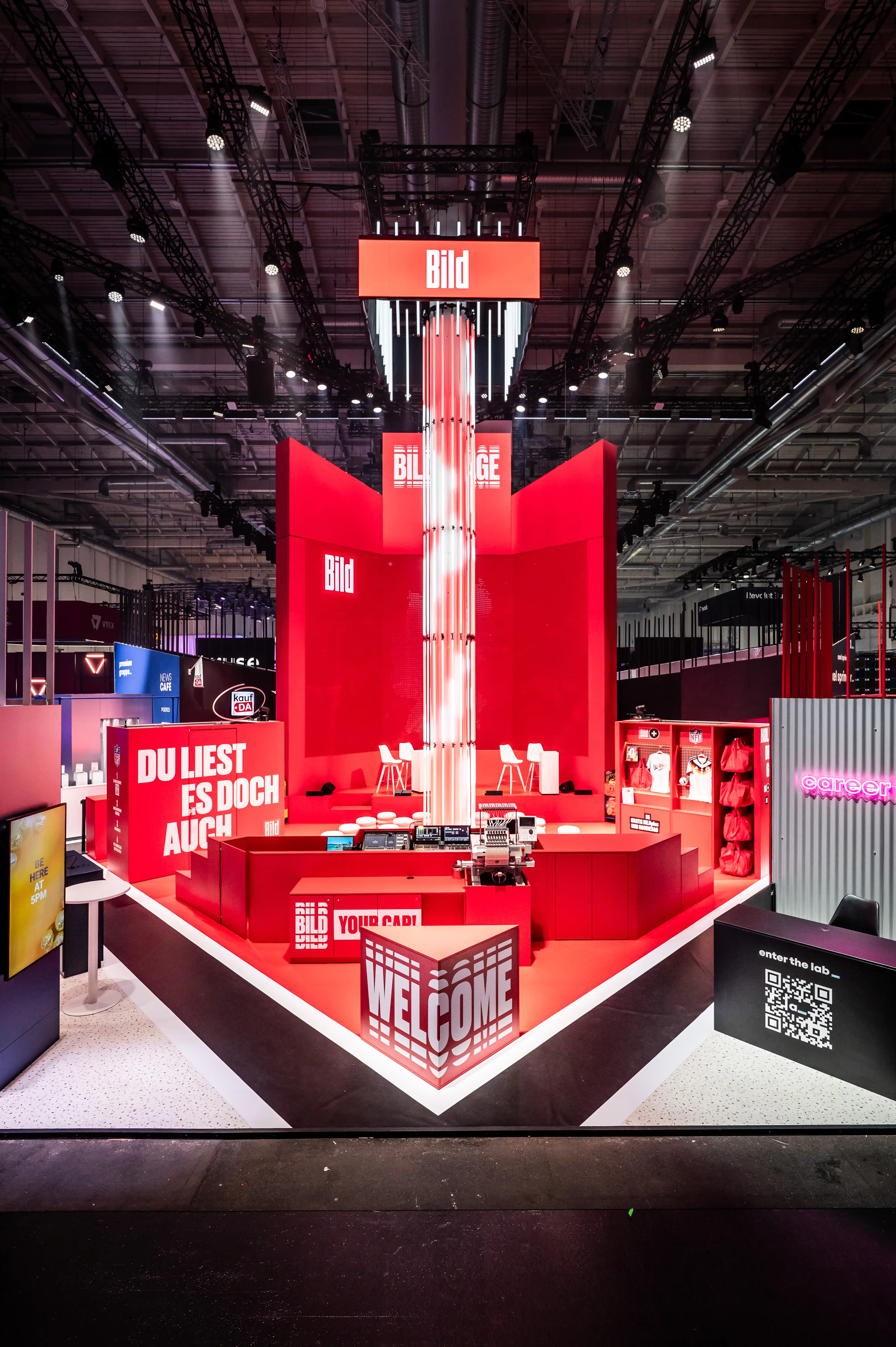 Tall red Bild booth tower with light column, slogan walls and Welcome counter at the front.