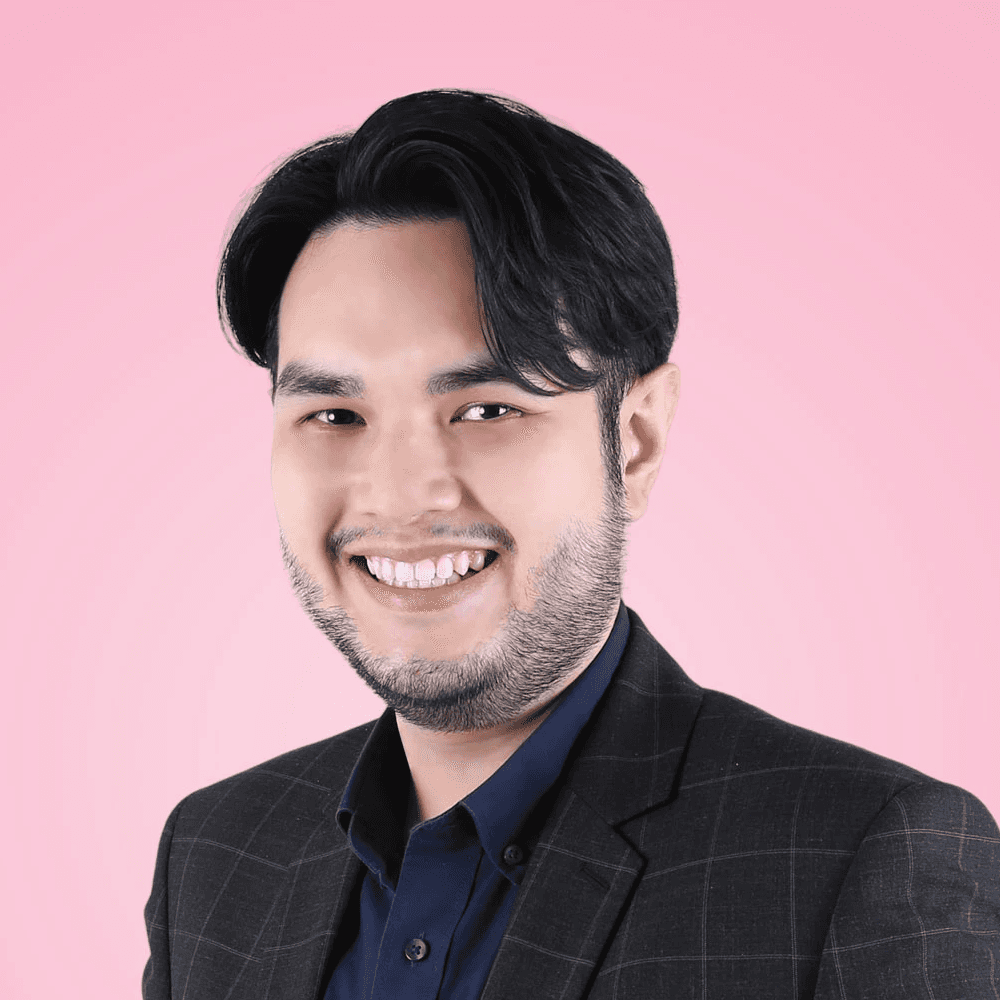 A smiling person with glasses, wearing a plaid shirt, against a purple background.