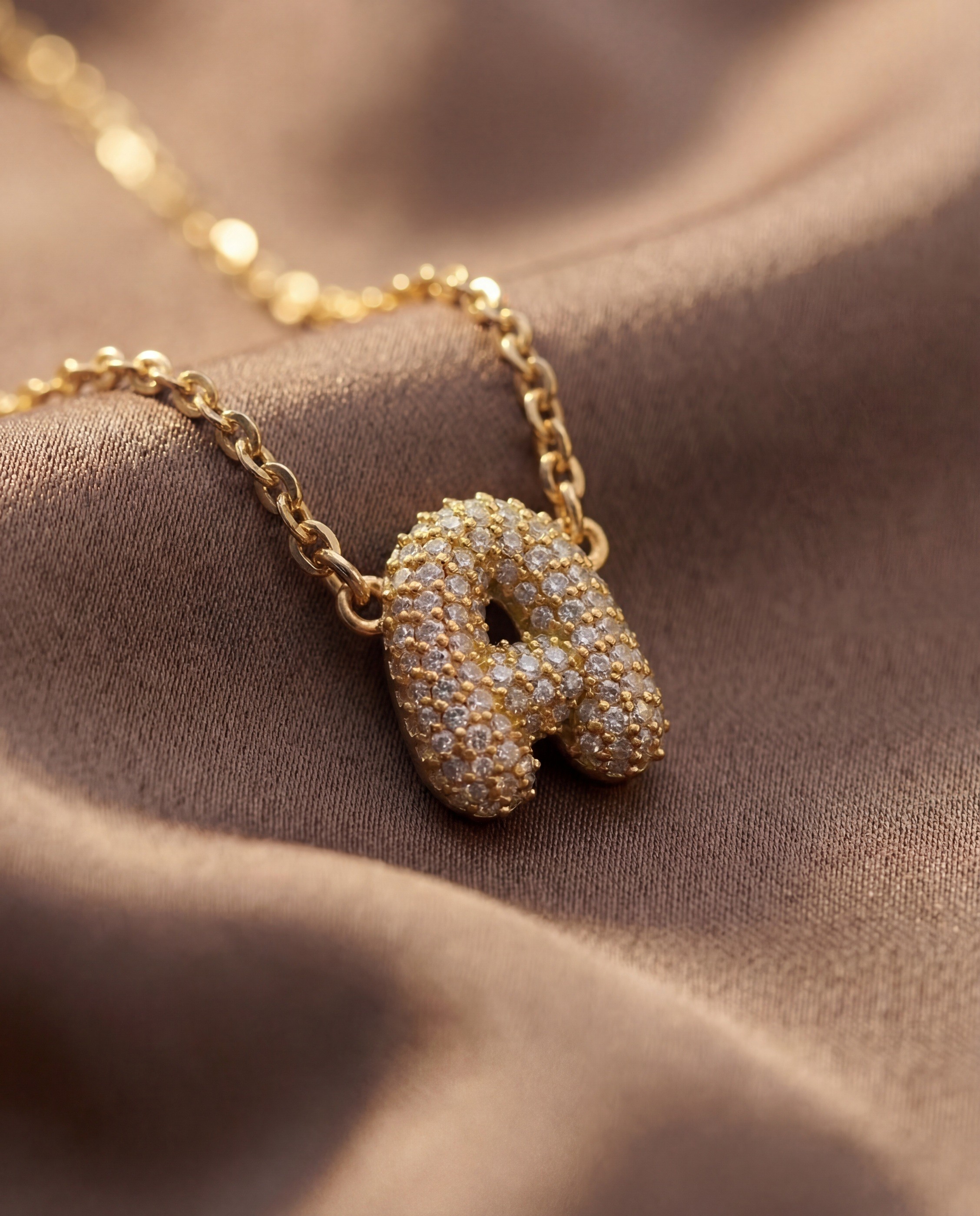 Vedder & Vedder — Pavé initial A pendant in close-up on warm brown fabric.