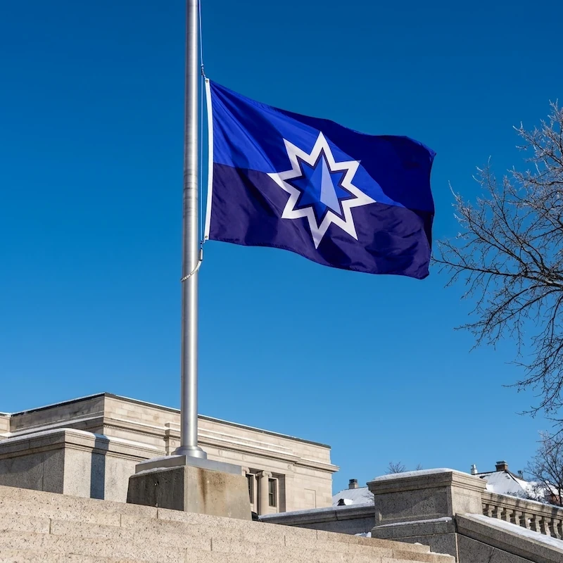 A blue flag with a large star in the middle flying on a flagpole against a cloudless blue sky