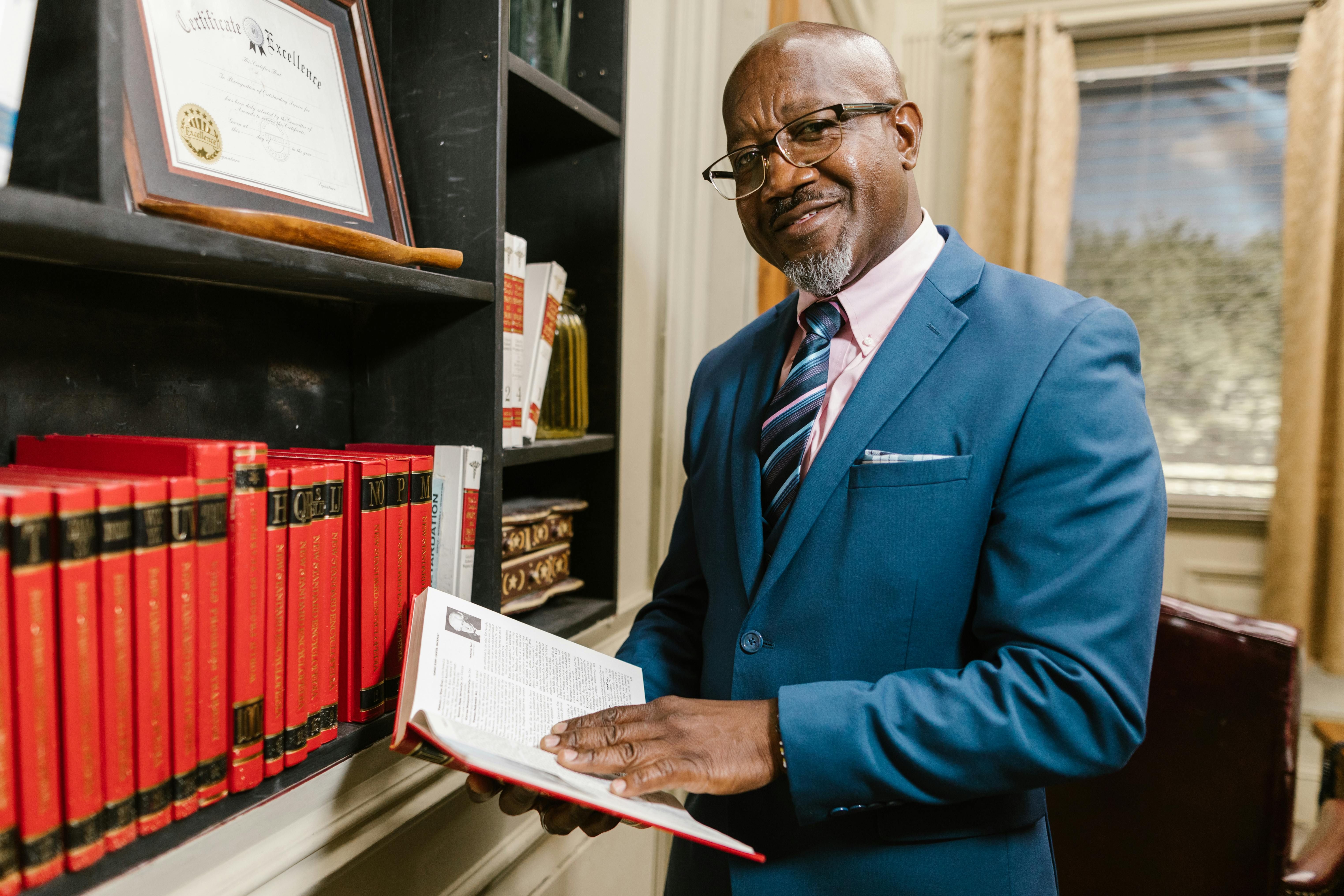 Professional man in blue suit holding book near office bookshelf