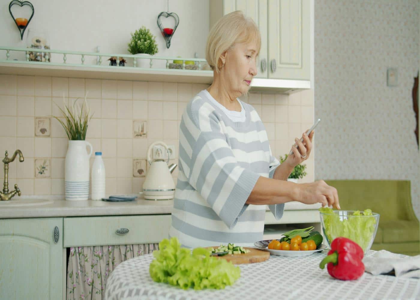 Older woman making a salad whilte looking at smartphone